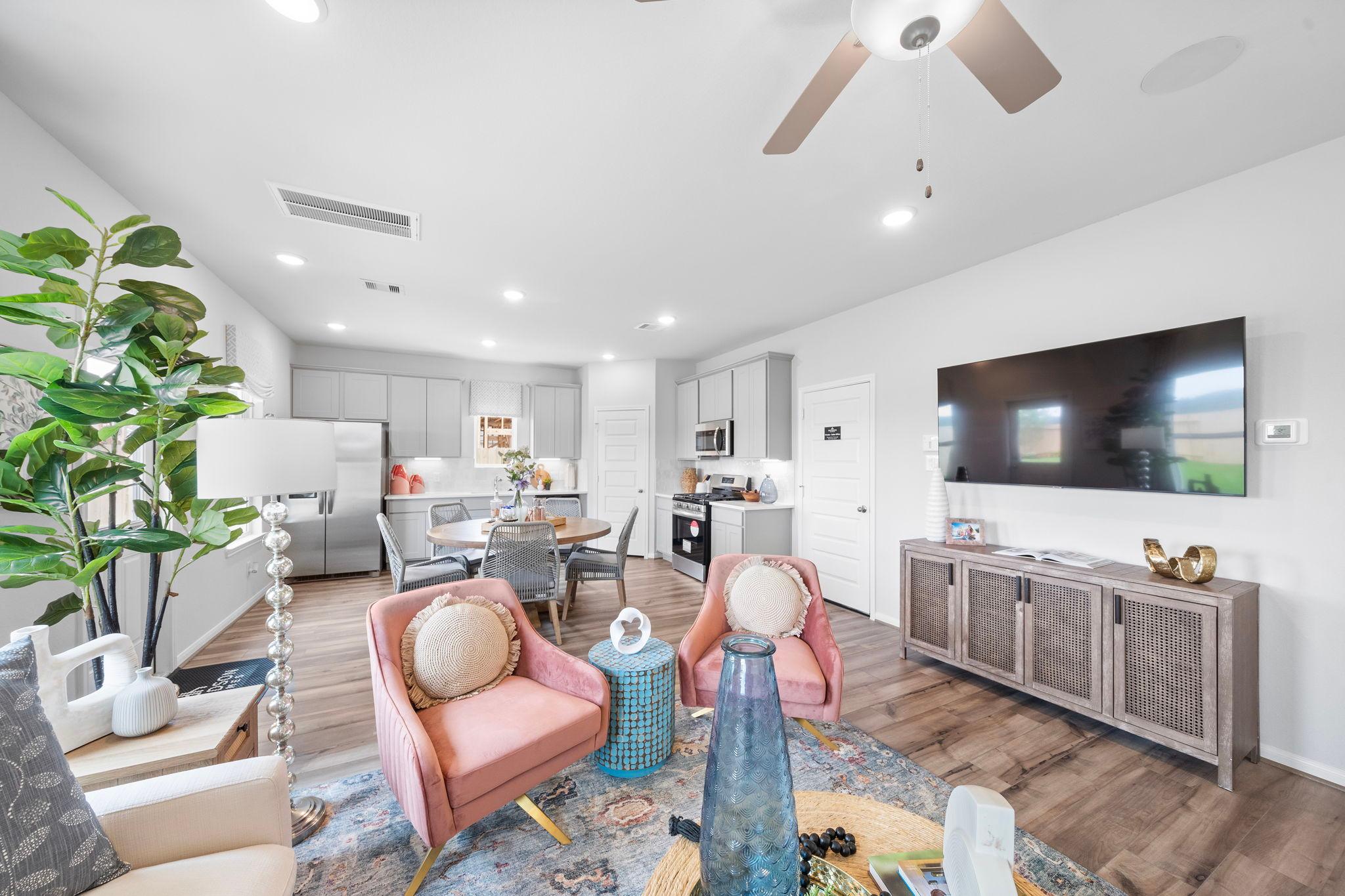 Spacious open-concept living and kitchen at Hill & Dale Ranch in Splendora Texas featuring pink armchairs hardwood floors white cabinets and wall TV