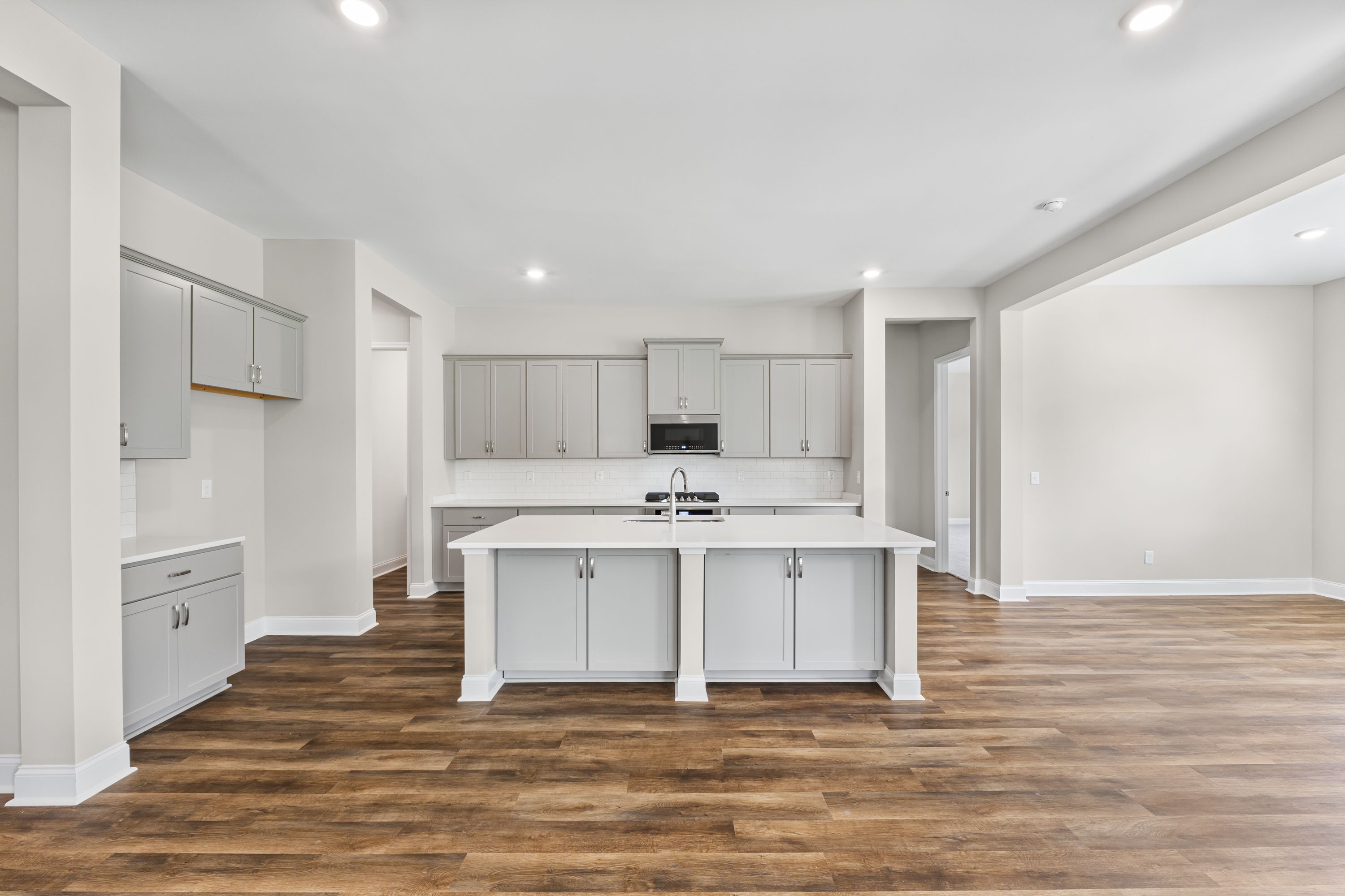Spacious kitchen in The Arcadia E with white shaker cabinets, large central island, quartz counters, and hardwood floors