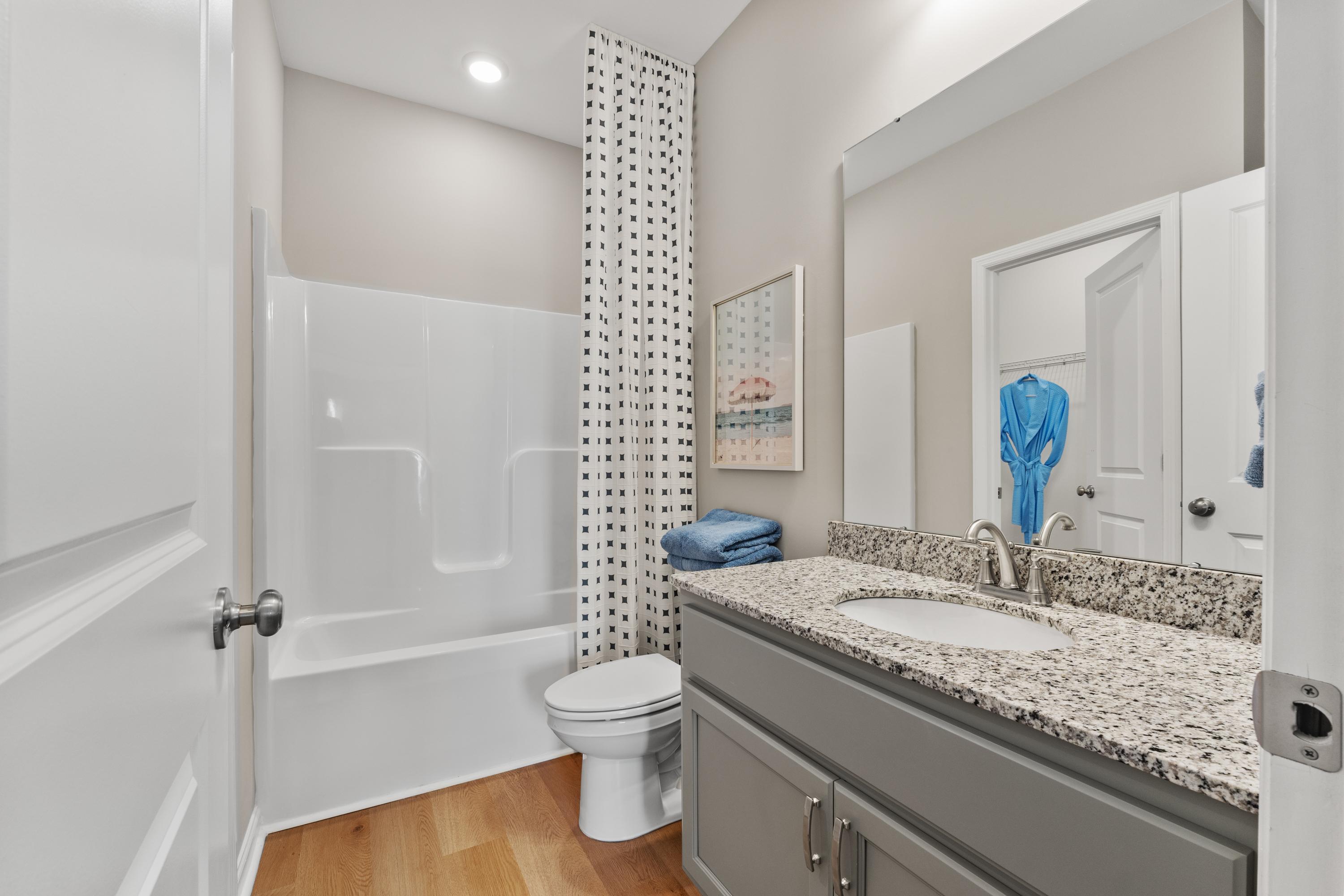 Guest bathroom at The Meadows at Hampton Cove in Owens Cross Roads AL with white tub-shower, gray vanity, granite countertop, blue towels