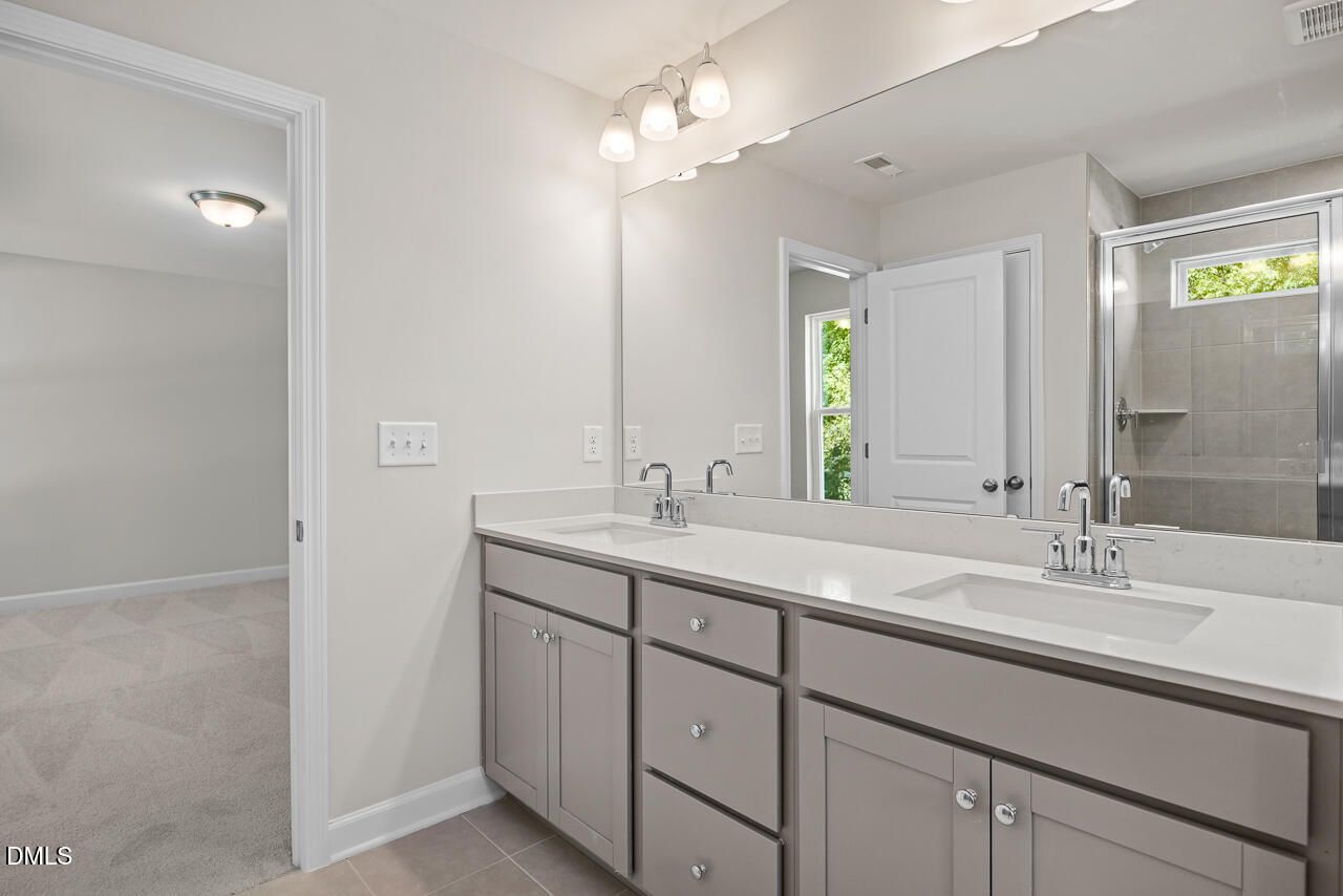Modern primary bathroom with double vanity, quartz countertops, and glass shower in The Gavin A home, Gregory Village, NC.