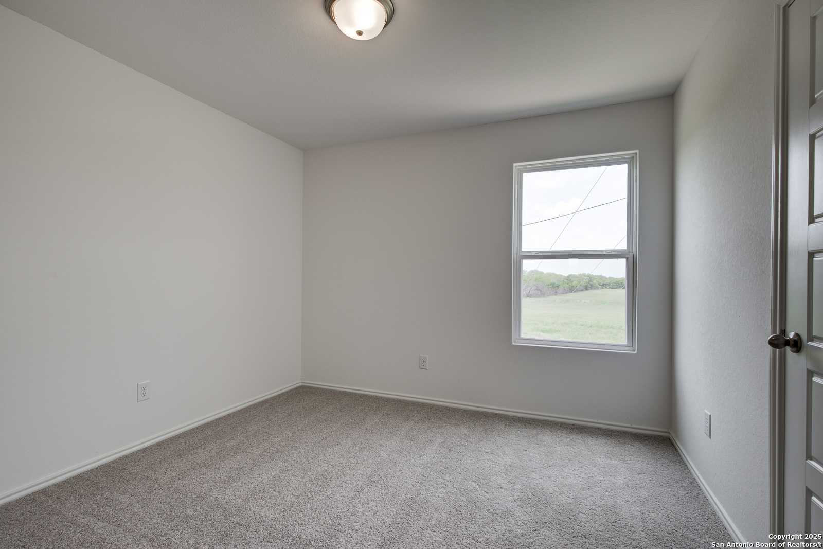 Bright secondary bedroom with white walls, gray carpet, and window overlooking green field in Davidson Homes Trinity A, San Antonio