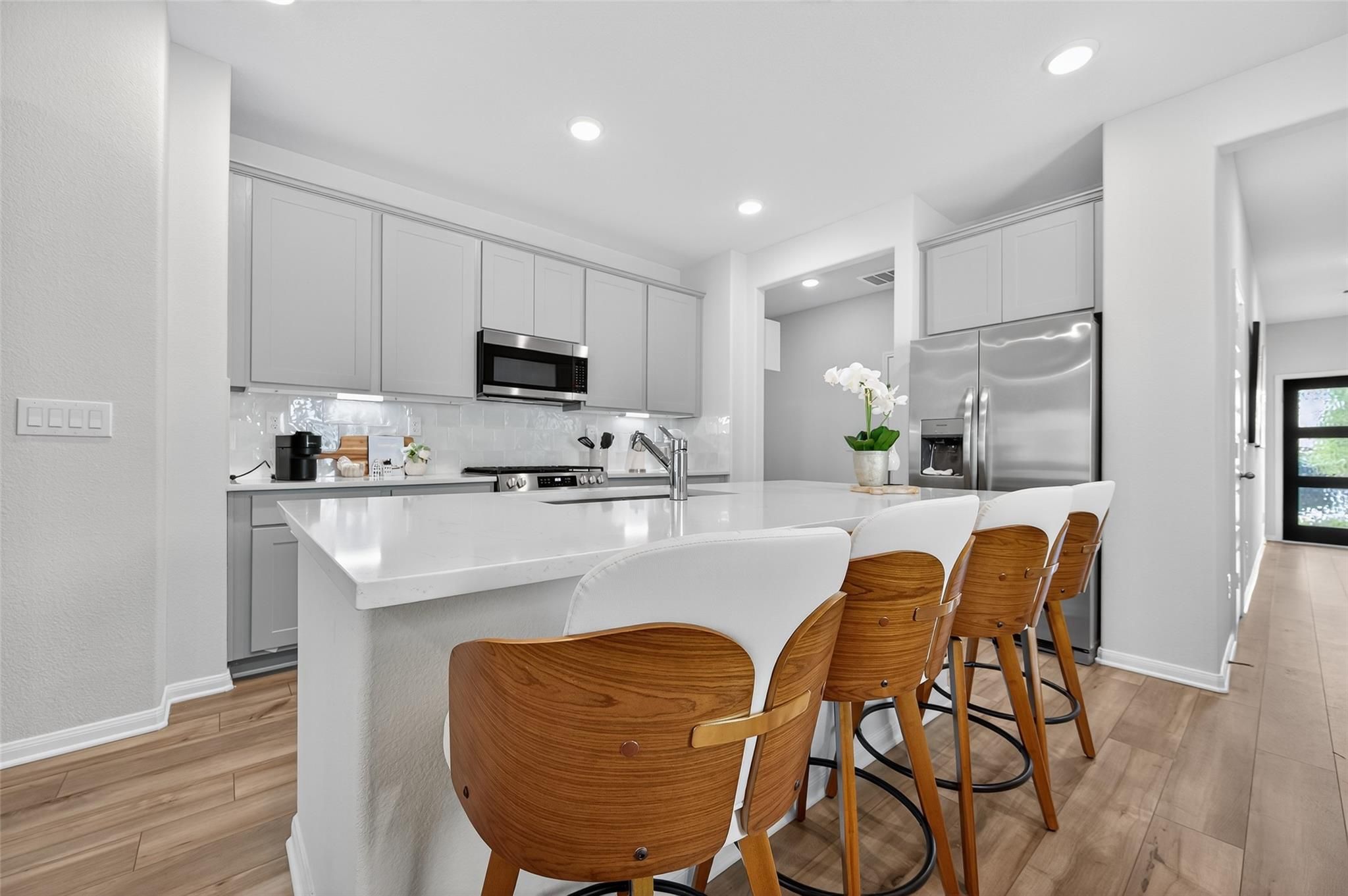 Modern white kitchen with quartz island, stainless appliances, wood bar stools in Davidson Homes Brazos E, Magnolia Texas