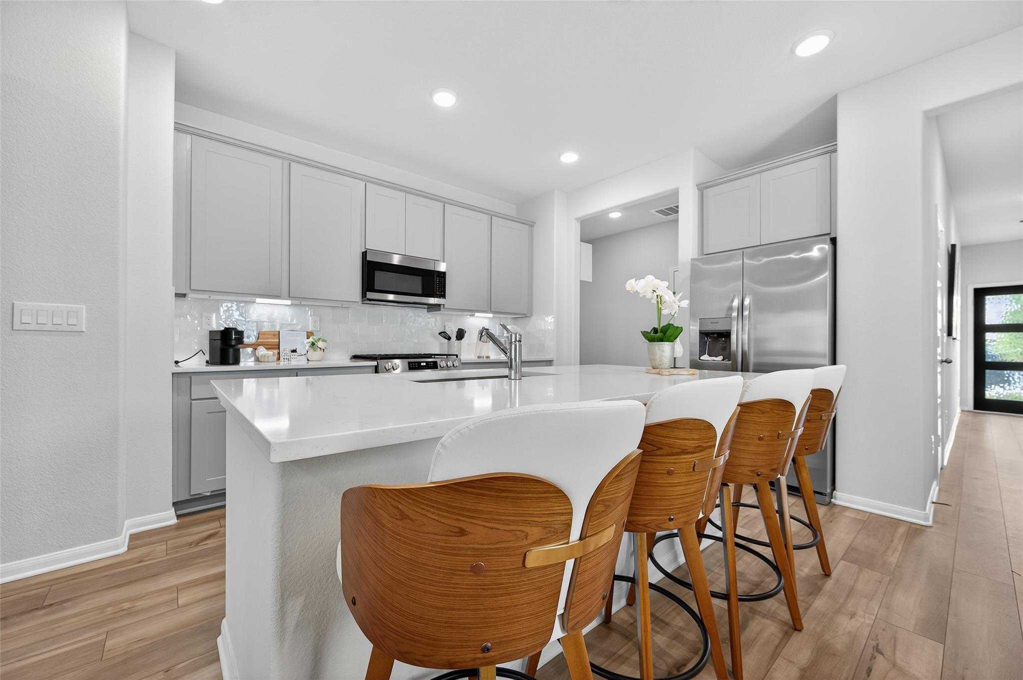Modern white kitchen with quartz island, stainless appliances, wood bar stools in Davidson Homes Brazos E, Magnolia Texas