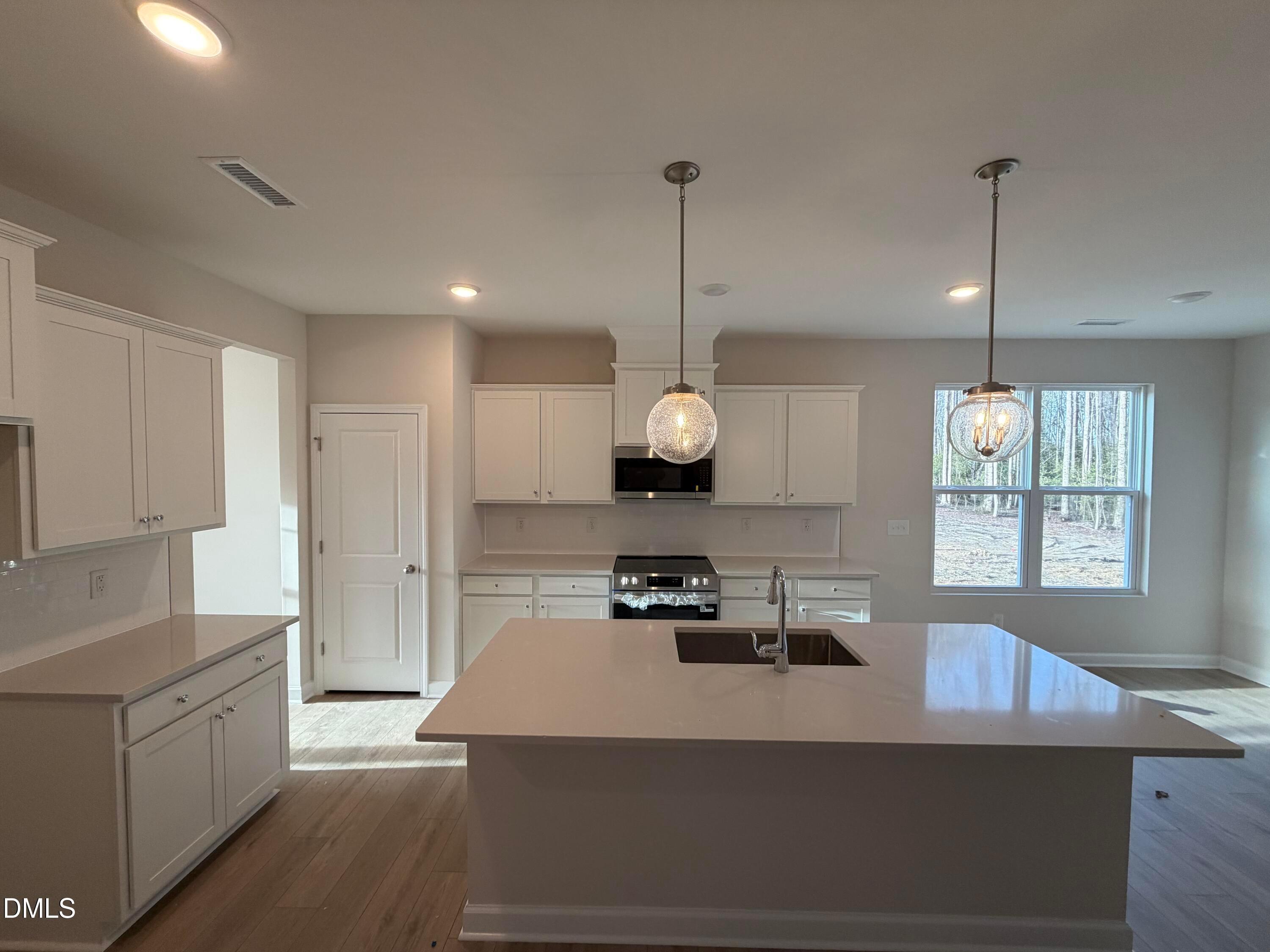 Modern kitchen with large white quartz island, shaker cabinets, stainless appliances, and pendant lights in Davidson Homes The Ash B, Lillington, NC