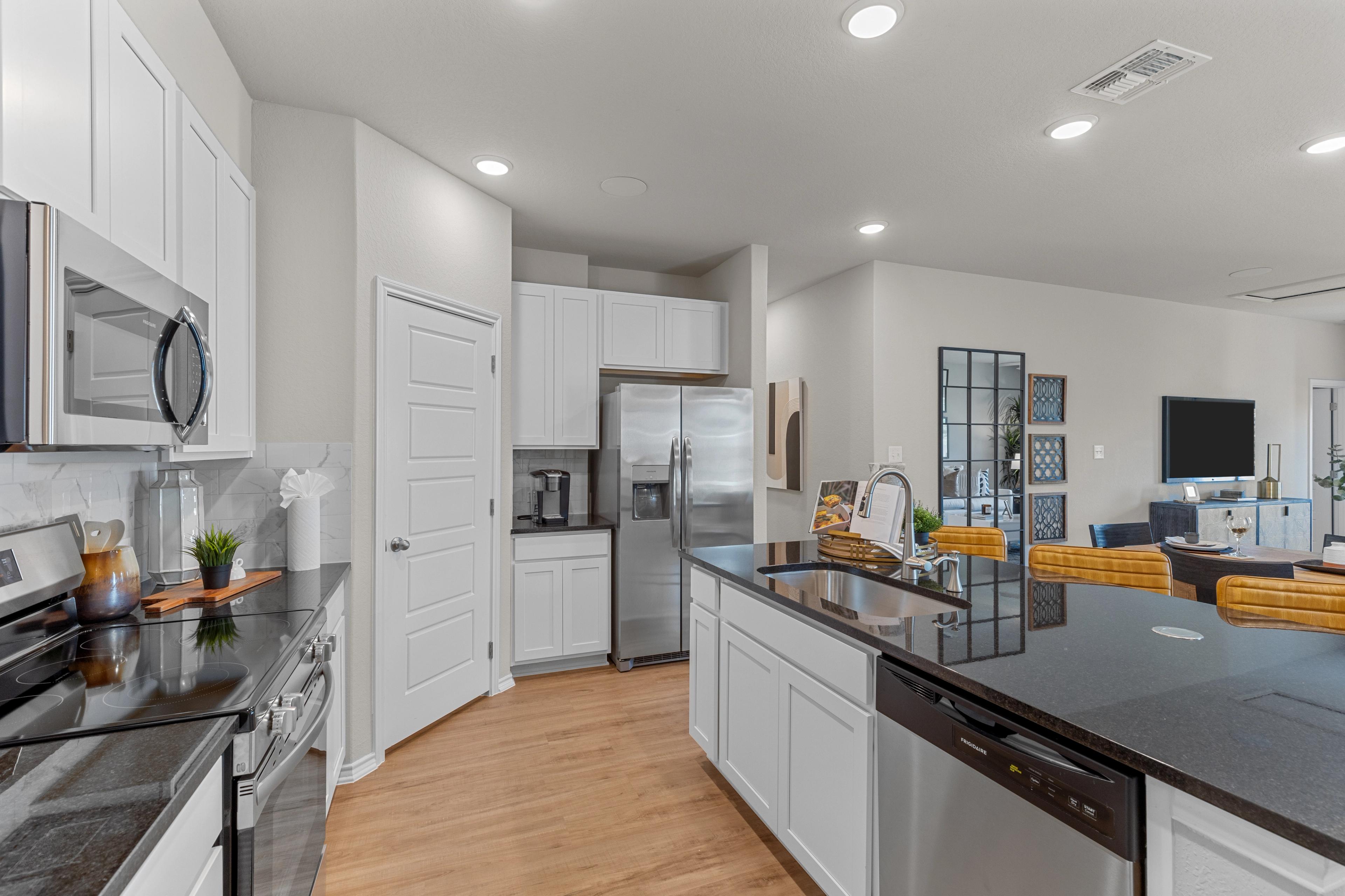 Modern Sabine B kitchen featuring white shaker cabinets, black granite island with sink, stainless steel appliances, and open layout