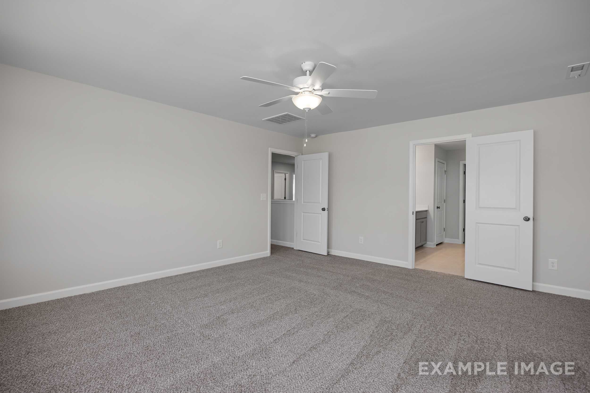 Spacious master bedroom in The Hickory II with gray carpet, ceiling fan, and open door to adjacent bath