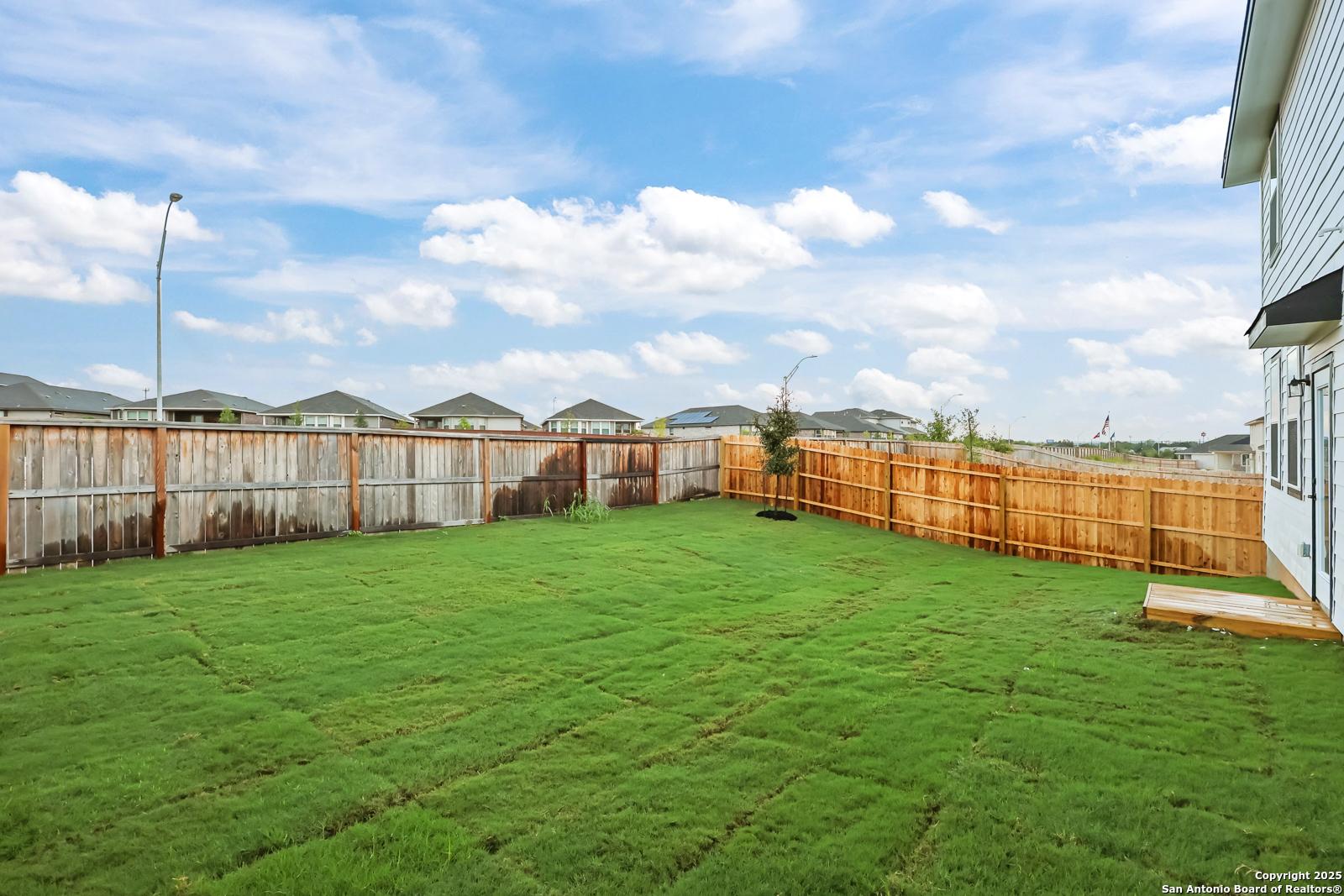 Private backyard with fresh sod, privacy fences, young trees, and covered patio in Davidson Homes The Douglas F, Comanche Ridge, San Antonio