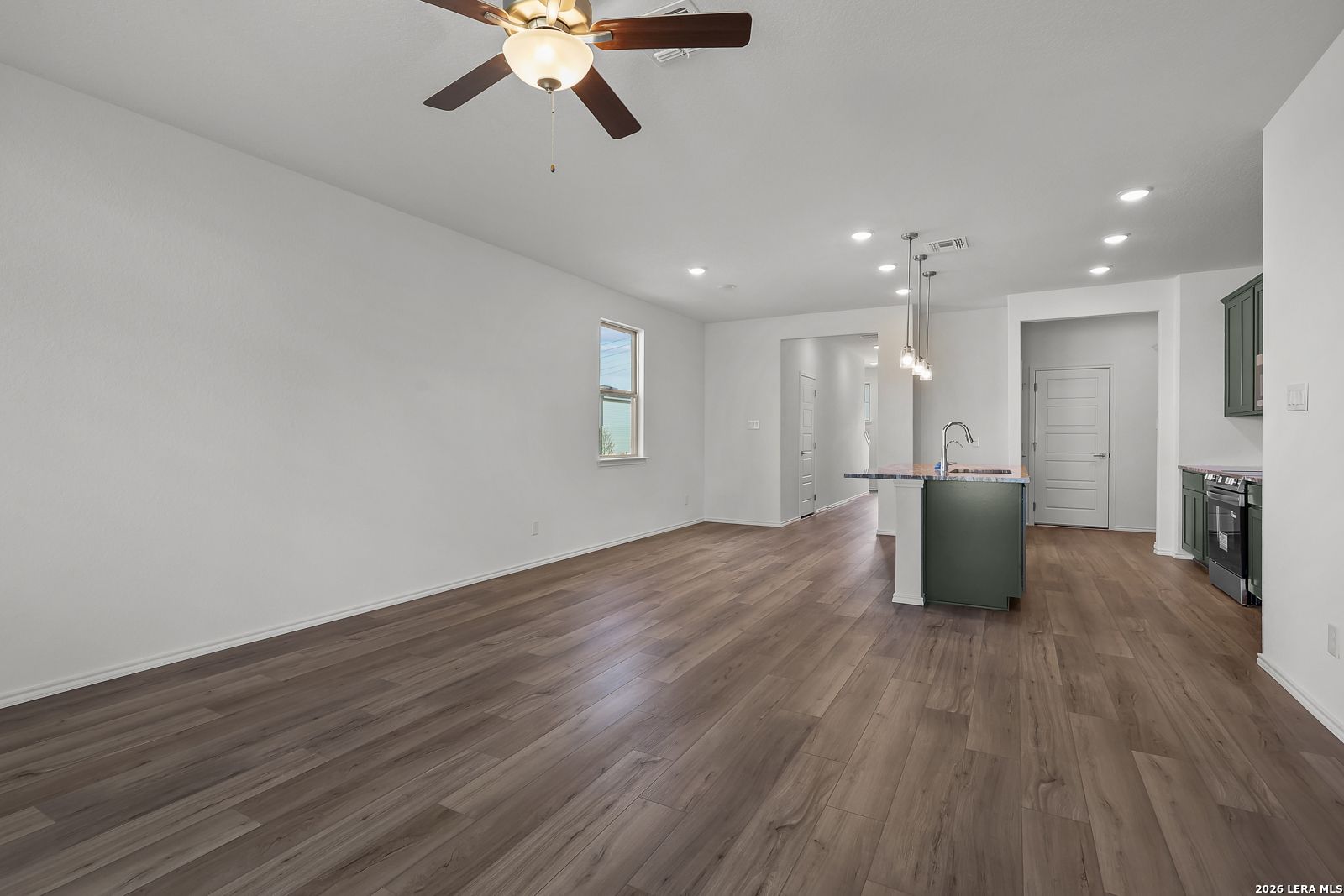 Open-concept living area with wood-look flooring and kitchen island in The Brazos B home in Agave, San Antonio, Texas.