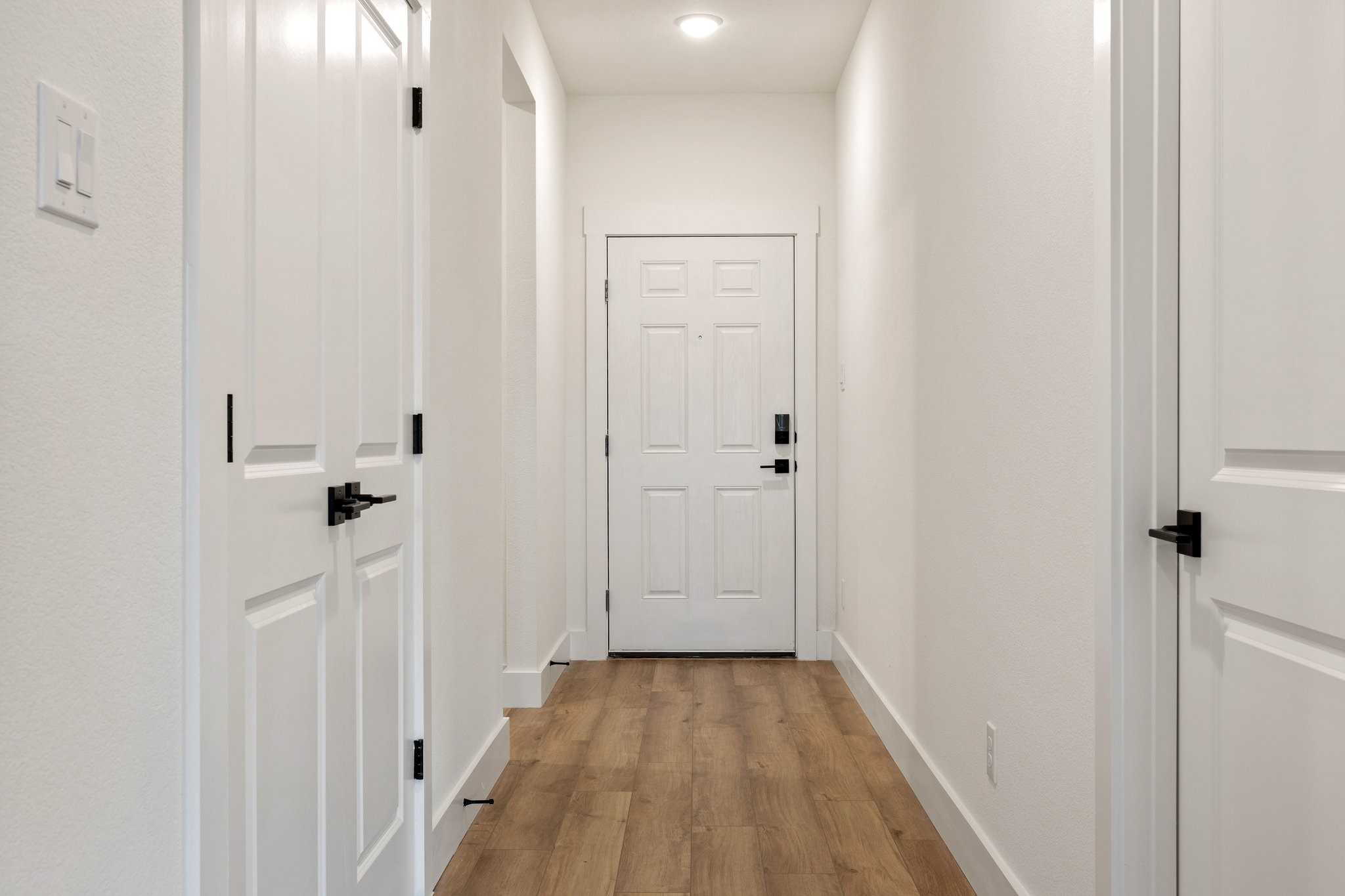 Bright hallway with white paneled doors, hardwood floors, and smart lock entry in The Rockford C home, Josephine, Texas