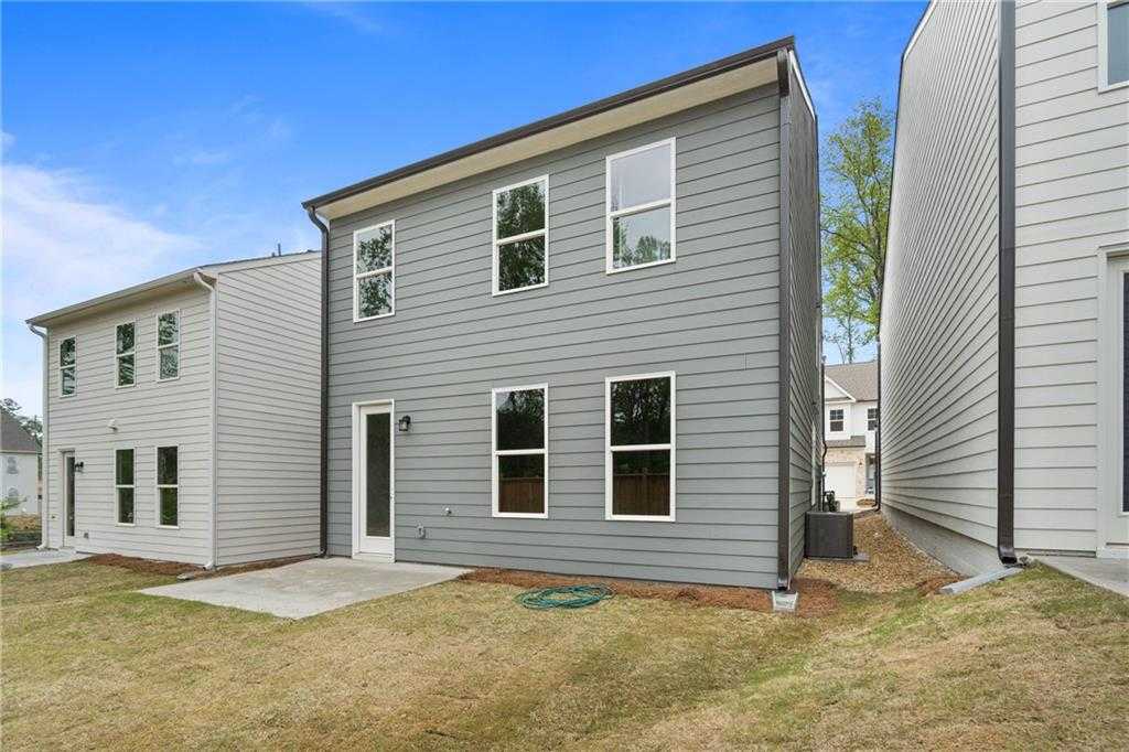 Two-story gray siding home exterior with back door, large windows, attached garage, and grassy backyard in The Village at Shallowford, Kennesaw, Georgia