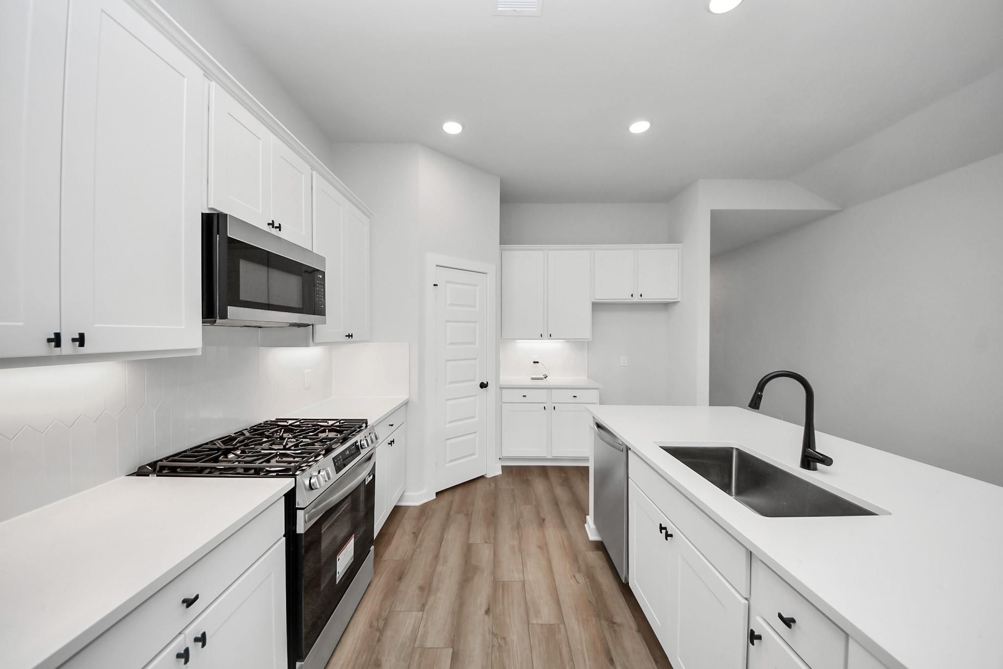 Modern white kitchen with stainless steel appliances and center island in The Riviera C home at River Ranch Meadows, Texas.