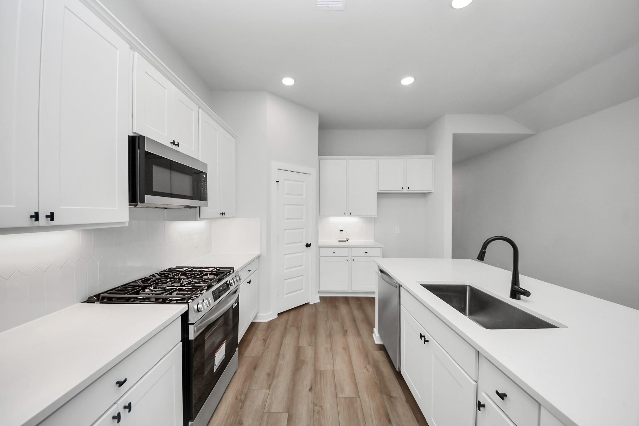Modern white kitchen with stainless steel appliances and center island in The Riviera C home at River Ranch Meadows, Texas.