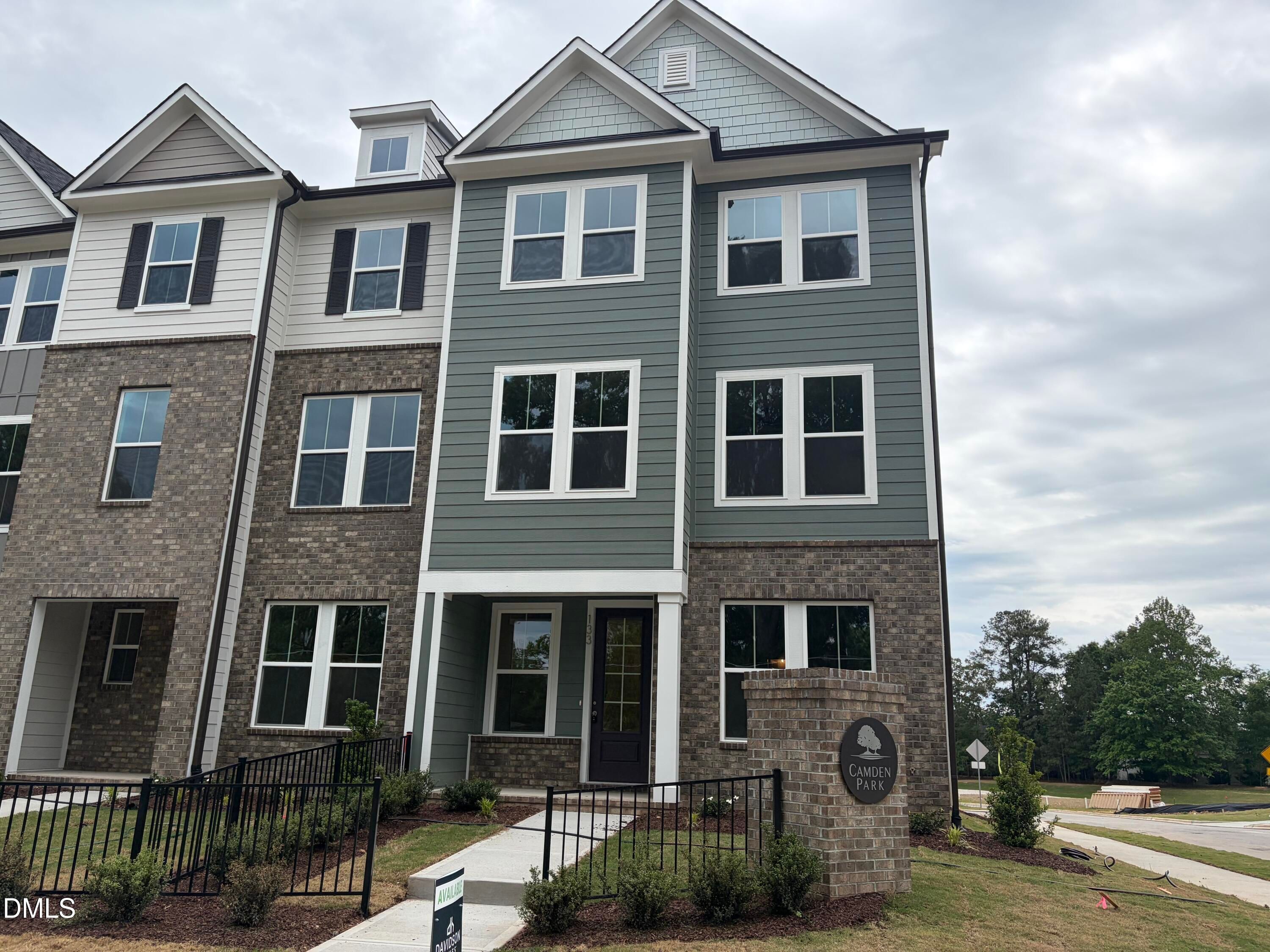 Modern three-story townhome with gray siding, brick accents, covered porch, and Camden Park sign in Knightdale, North Carolina by Davidson Homes