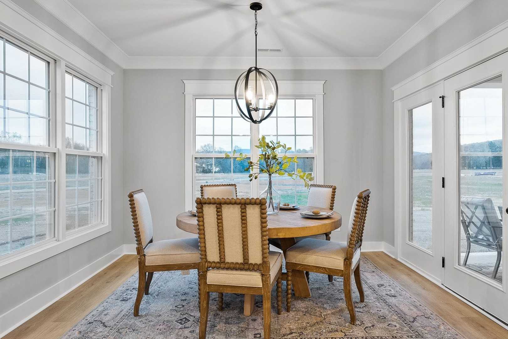 Spacious dining room in The Oxford featuring round wooden table, upholstered chairs, chandelier, and large windows