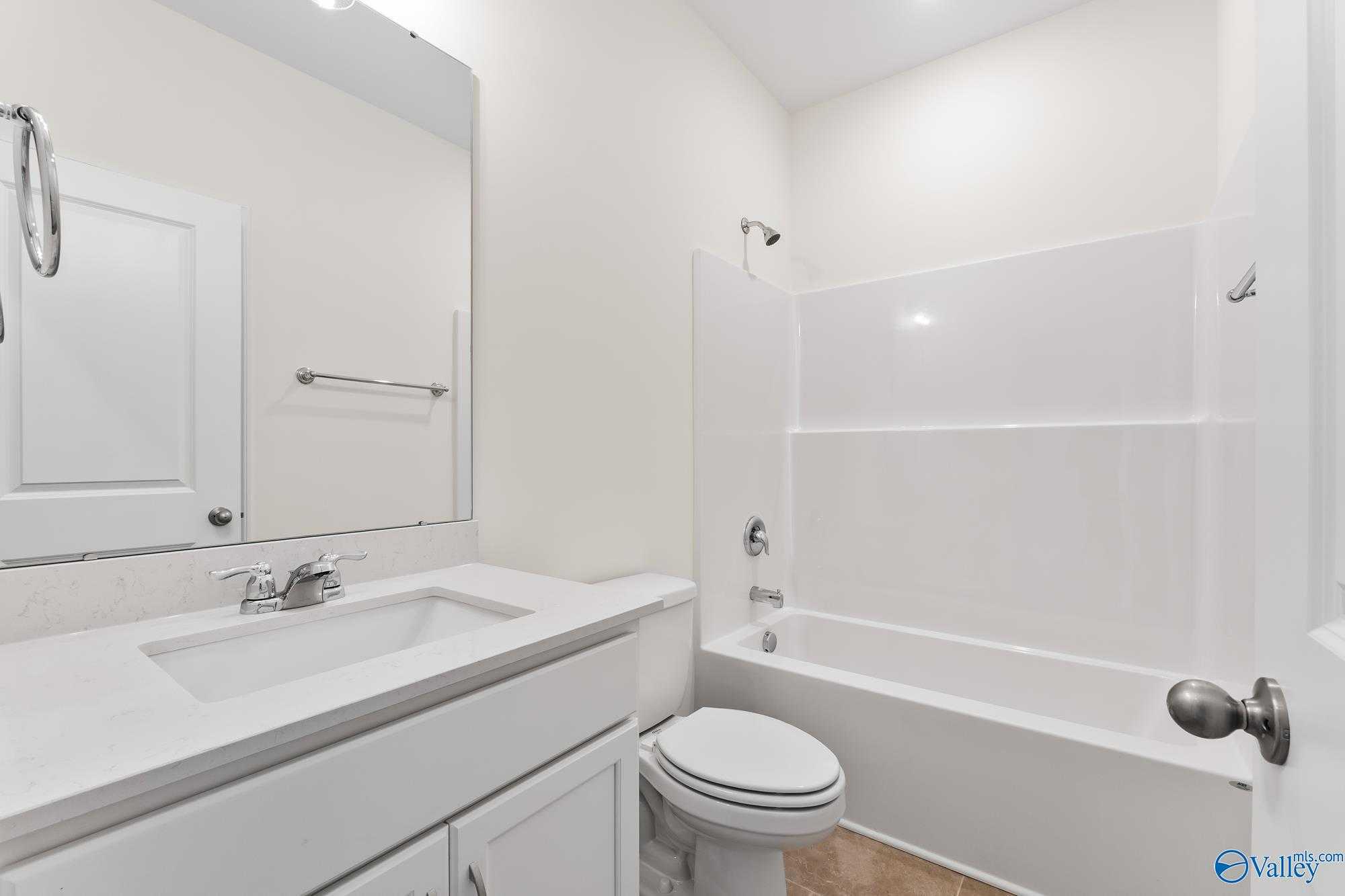 Bright guest bathroom with tub-shower combo, white vanity sink, and toilet in 4-bedroom The Harrison home by Davidson Homes, Meridianville, Alabama
