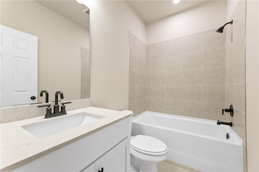 Bright bathroom with beige tiled shower-tub combo, white vanity, and modern fixtures in Davidson Homes The Harrison H, Winder GA