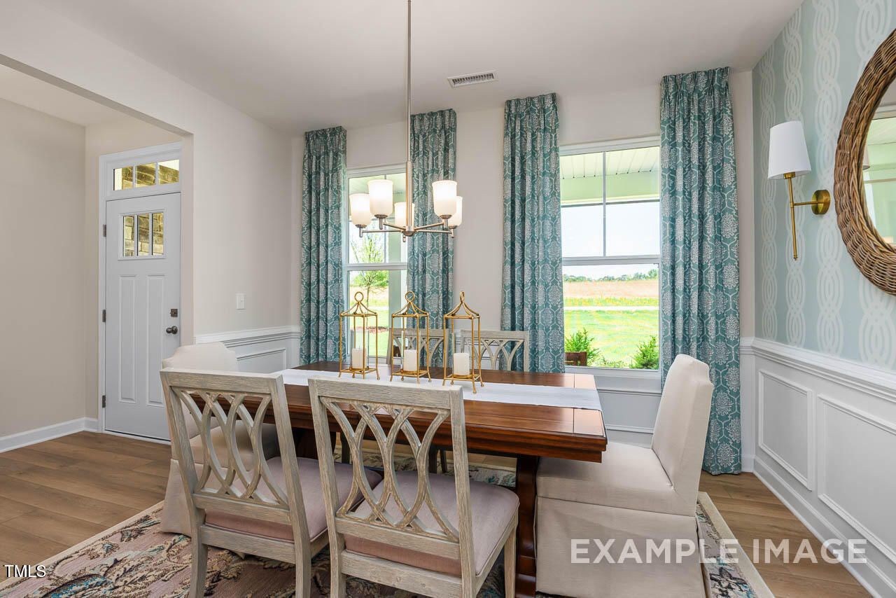 Elegant dining room with wooden table, chandelier, blue curtains, and field views in The Willow G 5-bedroom home by Davidson Homes, Angier, NC