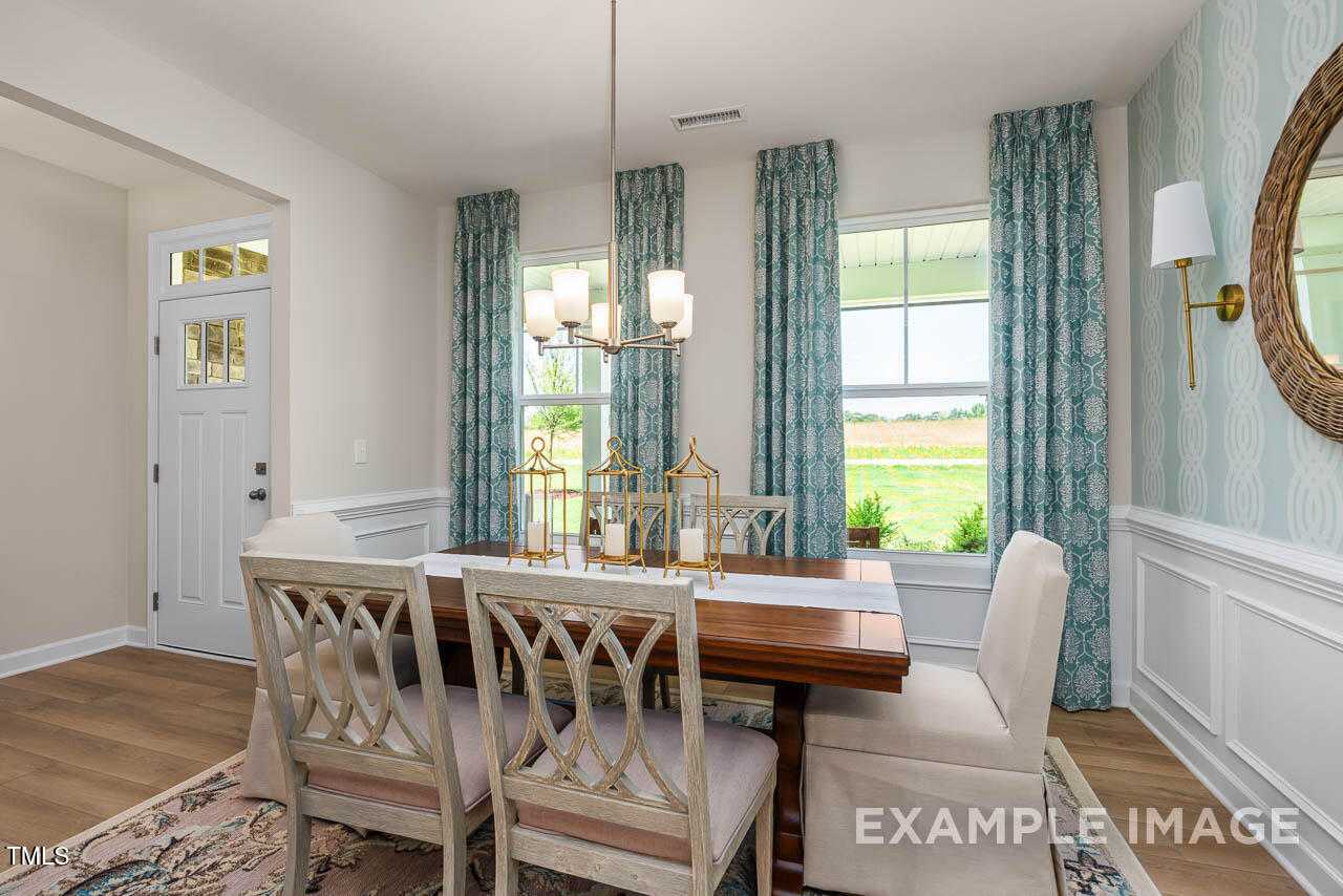 Elegant dining room with wooden table, upholstered chairs, chandelier, and garden views in Davidson Homes The Willow C, Angier, NC