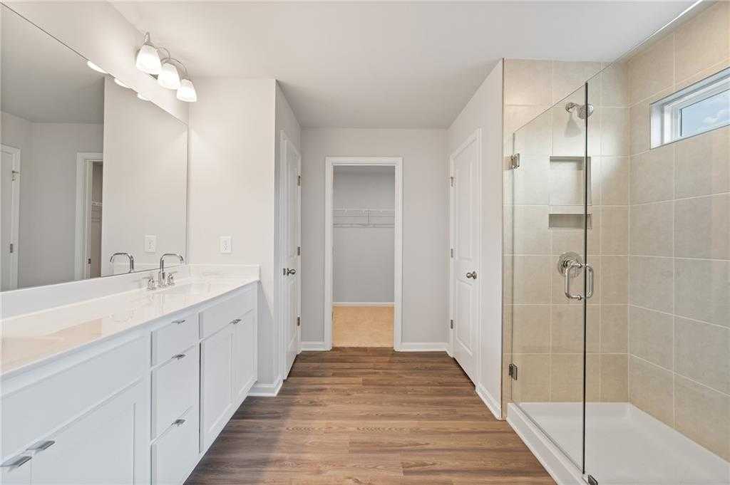Modern master bathroom with white double vanity, frameless glass shower, and walk-in closet in Davidson Homes The Hickory B, Winder, GA