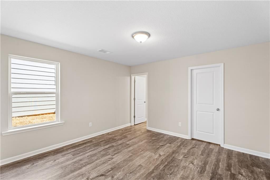 Bright secondary bedroom with beige walls, large window blinds, ceiling light, and wood-look flooring in Davidson Homes The Washington, Phenix City