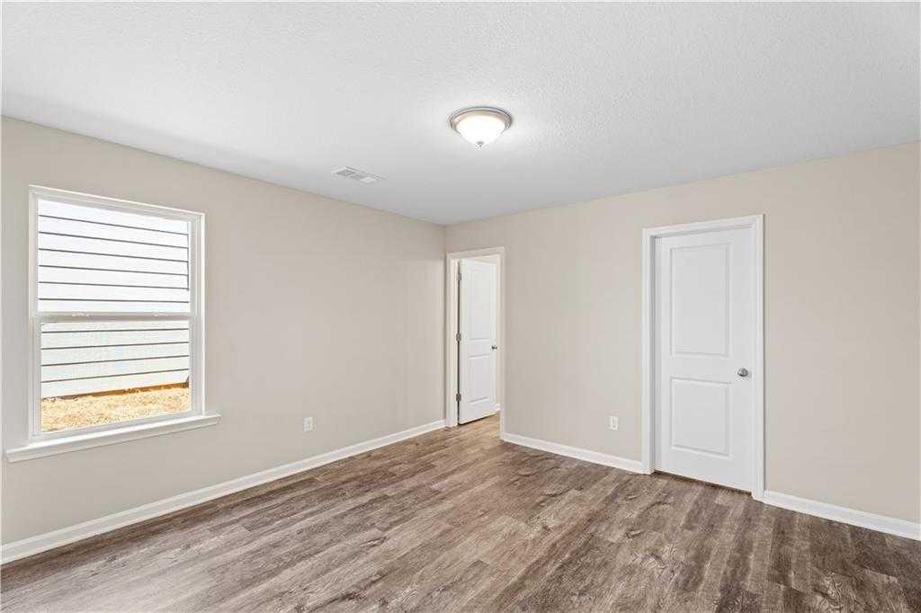 Bright secondary bedroom with beige walls, large window blinds, ceiling light, and wood-look flooring in Davidson Homes The Washington, Phenix City