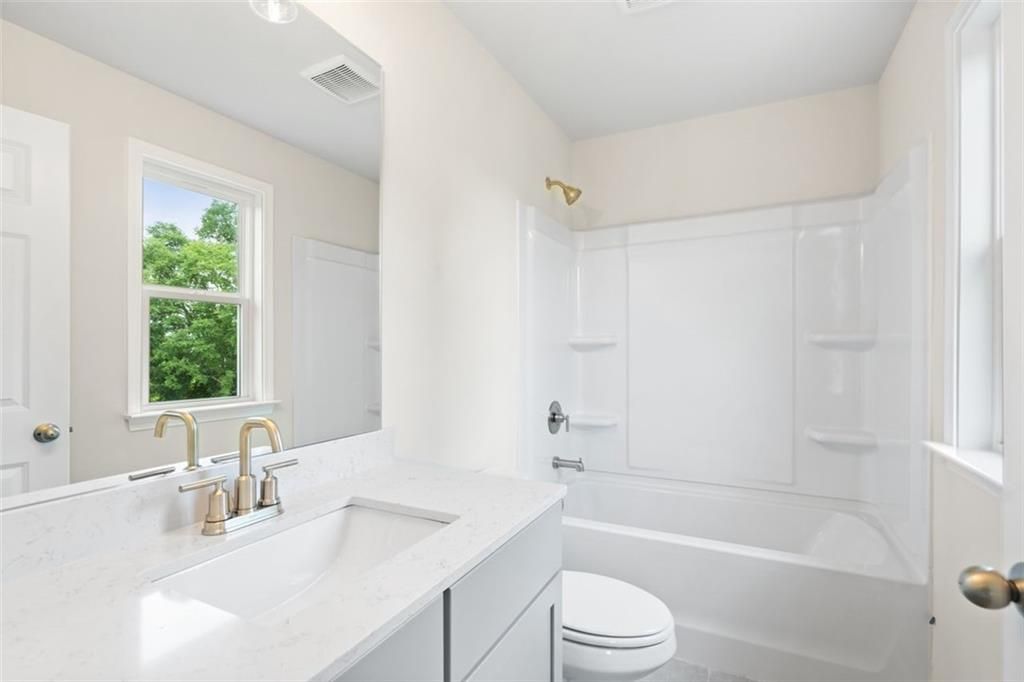 Bright bathroom with white tub-shower combo, quartz vanity, gold fixtures in Davidson Homes The Willow B, Hoschton, Georgia