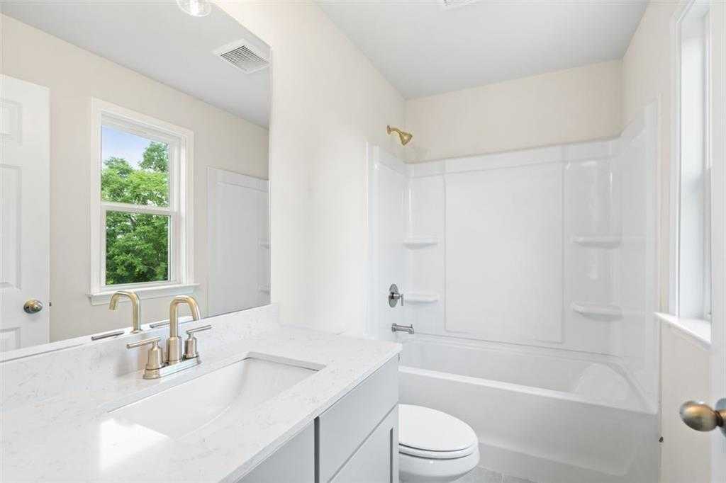 Bright bathroom with white tub-shower combo, quartz vanity, gold fixtures in Davidson Homes The Willow B, Hoschton, Georgia