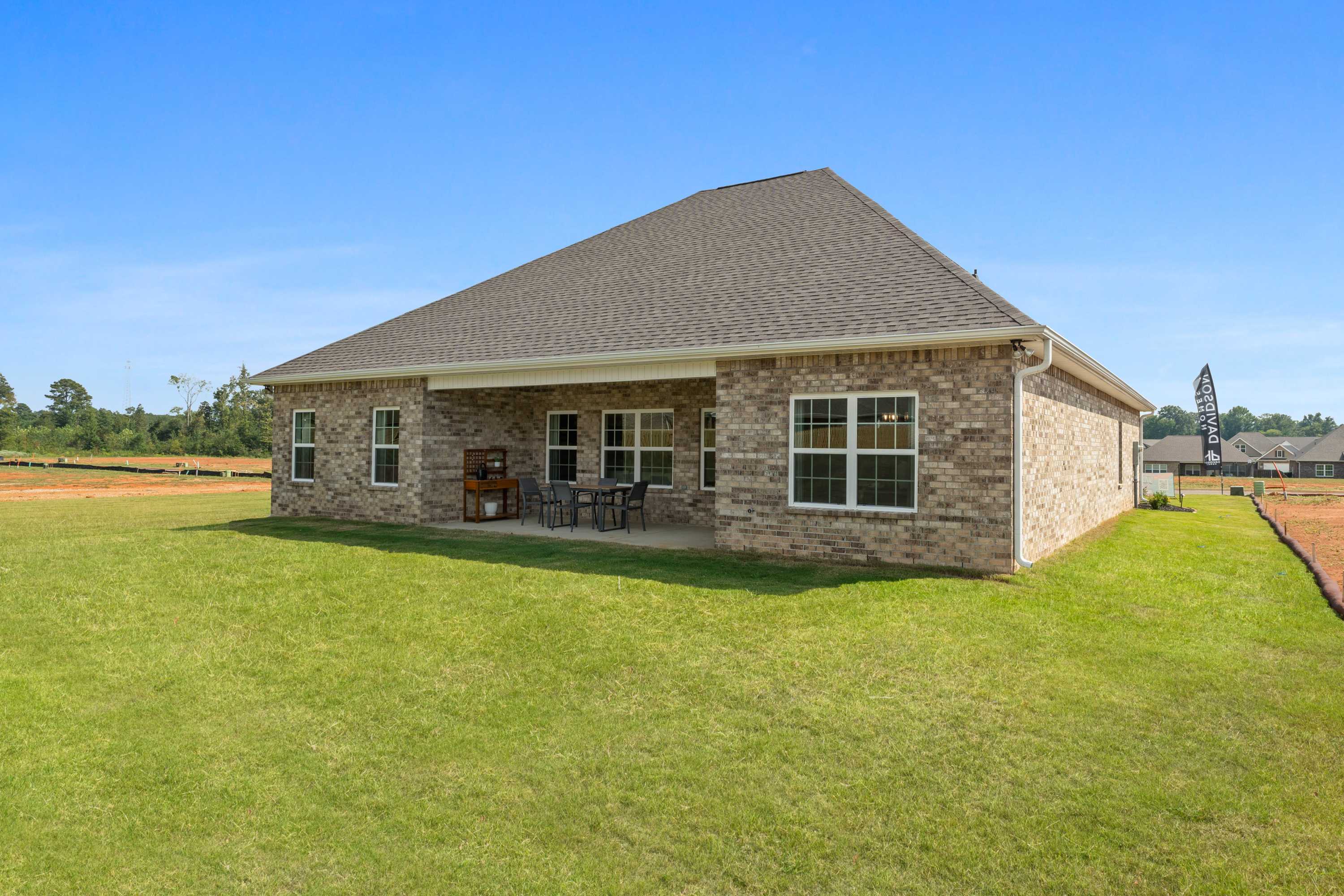 Brick home rear exterior with covered patio, outdoor seating, and lush green lawn at River Road Estates in Decatur, Alabama