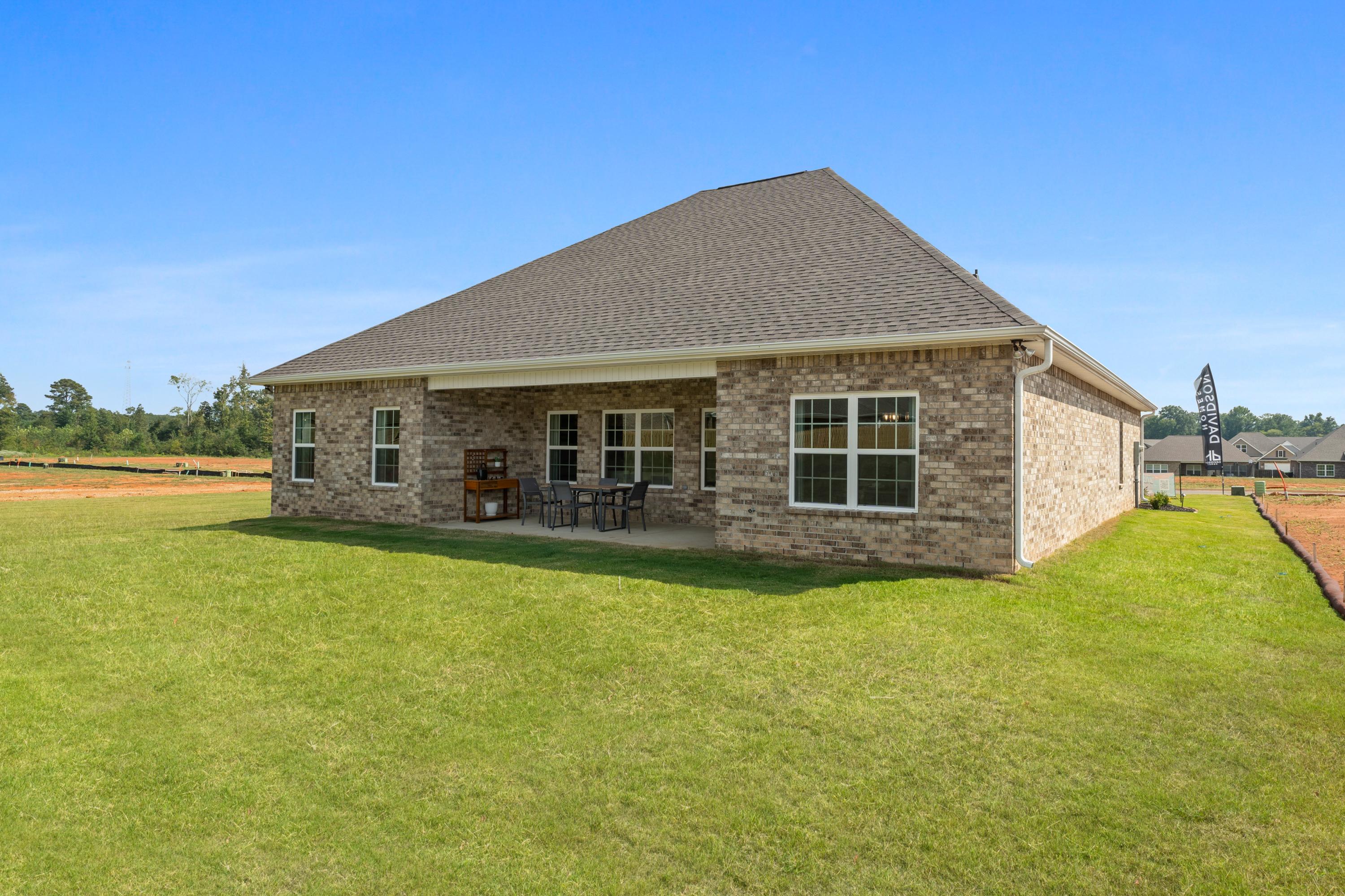 Brick home rear exterior with covered patio, outdoor seating, and lush green lawn at River Road Estates in Decatur, Alabama