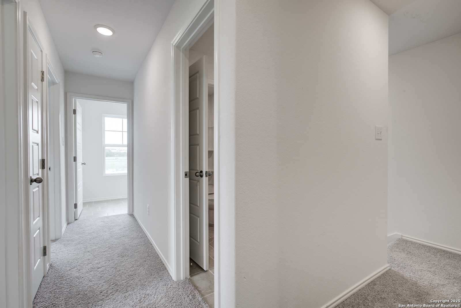 Bright carpeted hallway with white walls and open bedroom doors in Davidson Homes The Trinity A, San Antonio