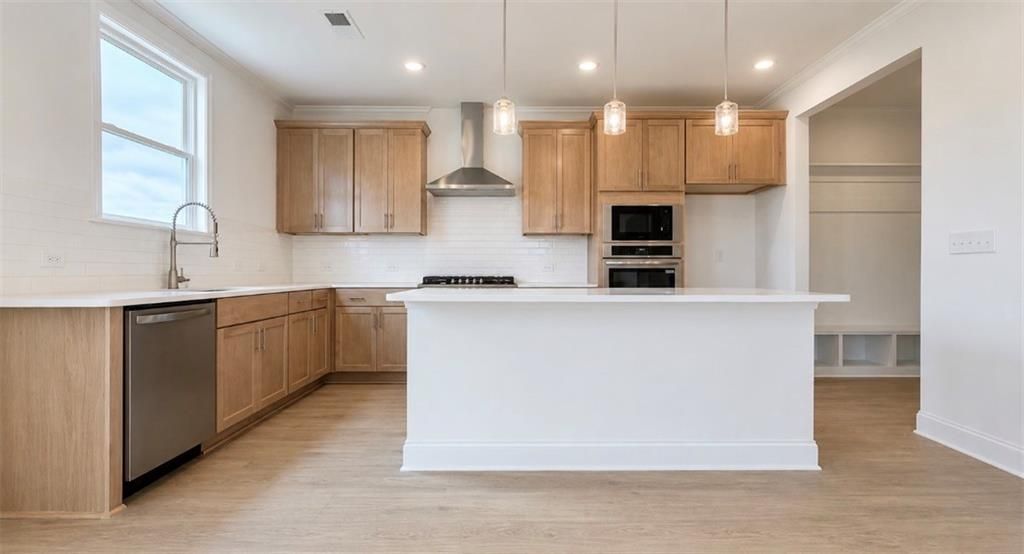 Modern kitchen with light wood cabinets, white island, and stainless appliances in The Hickory C floor plan, Wehunt Meadows.