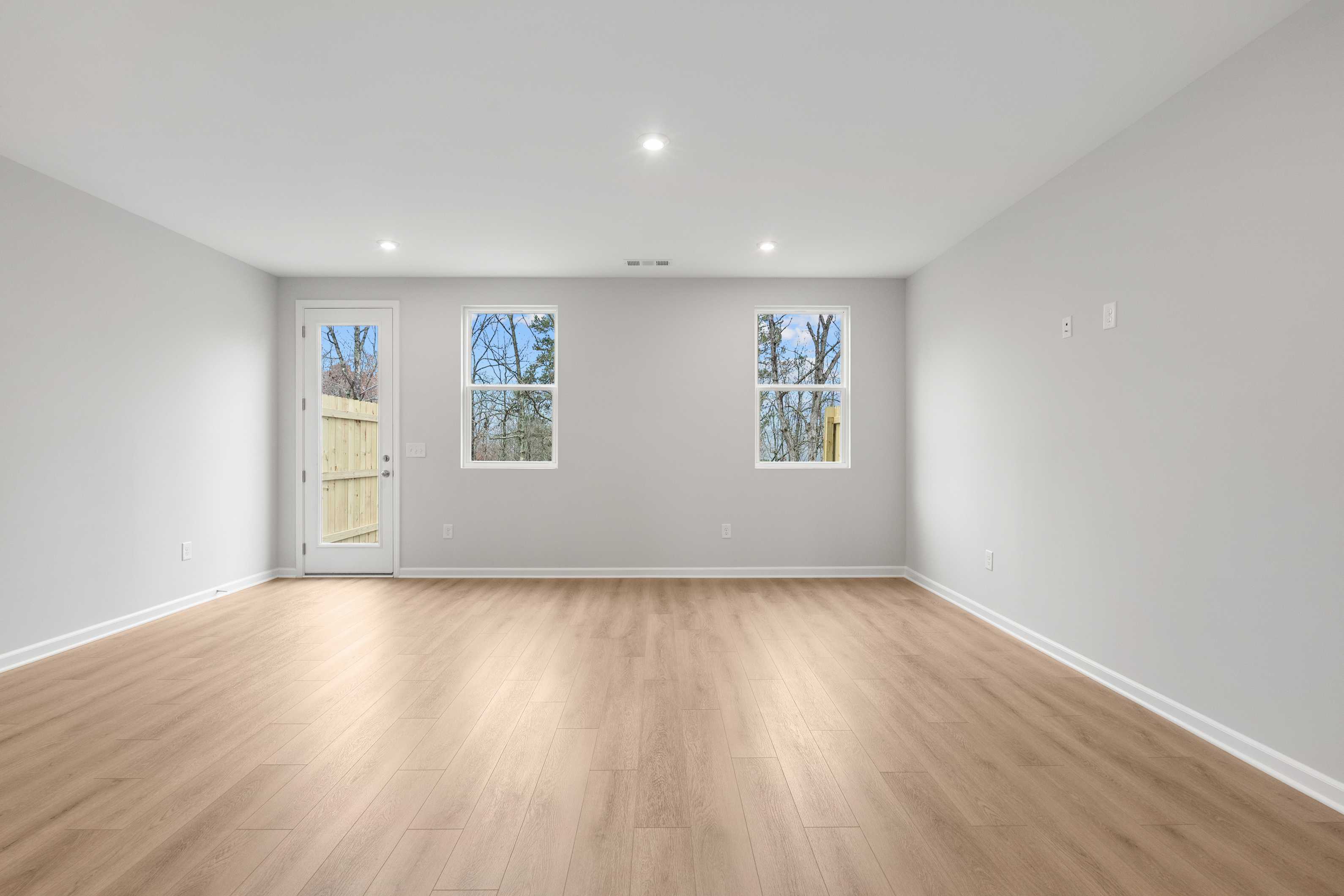 Spacious empty interior room in The Durant A with light gray walls, hardwood floors, large windows, and glass door