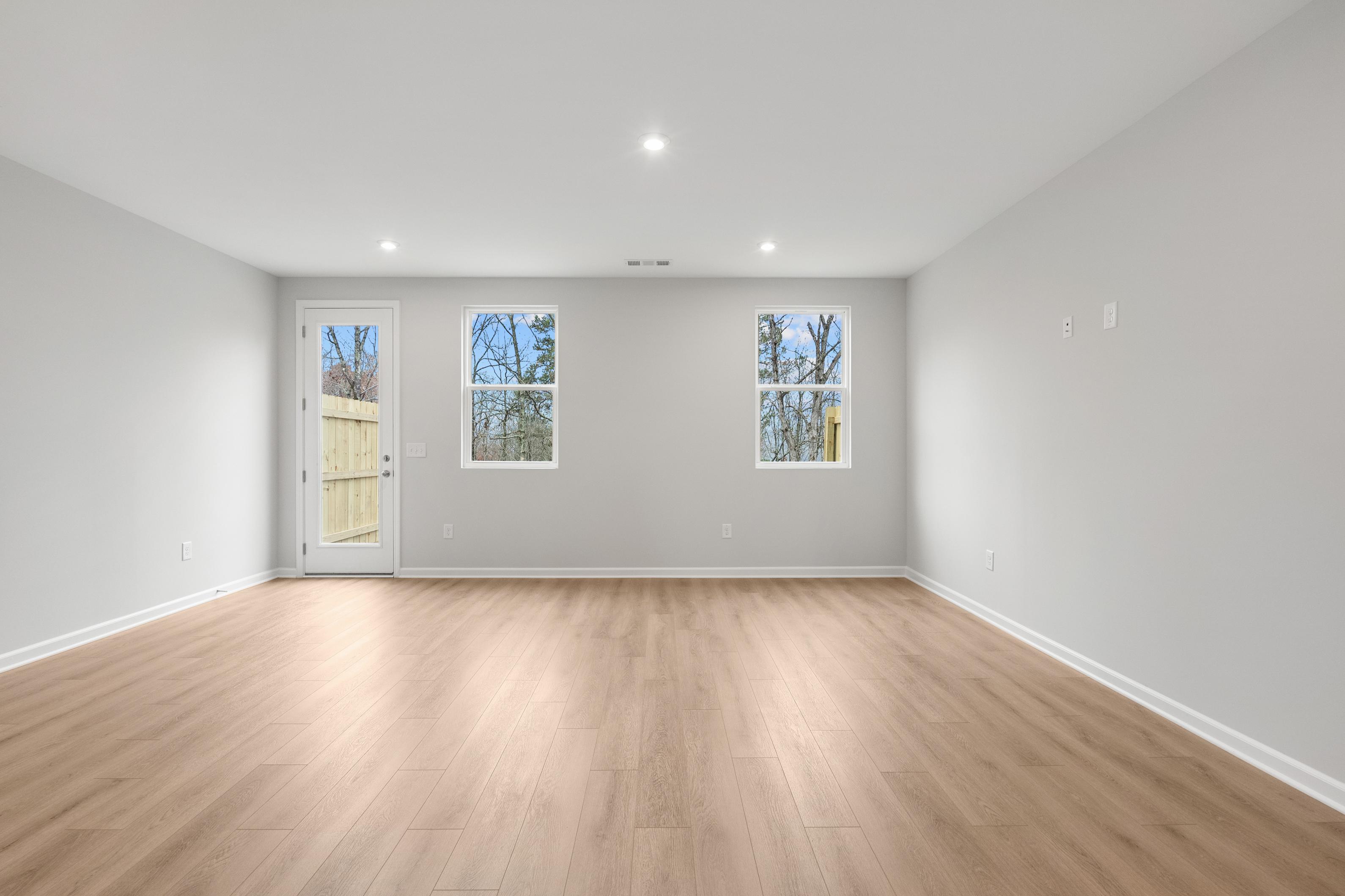 Spacious empty interior room in The Durant A with light gray walls, hardwood floors, large windows, and glass door