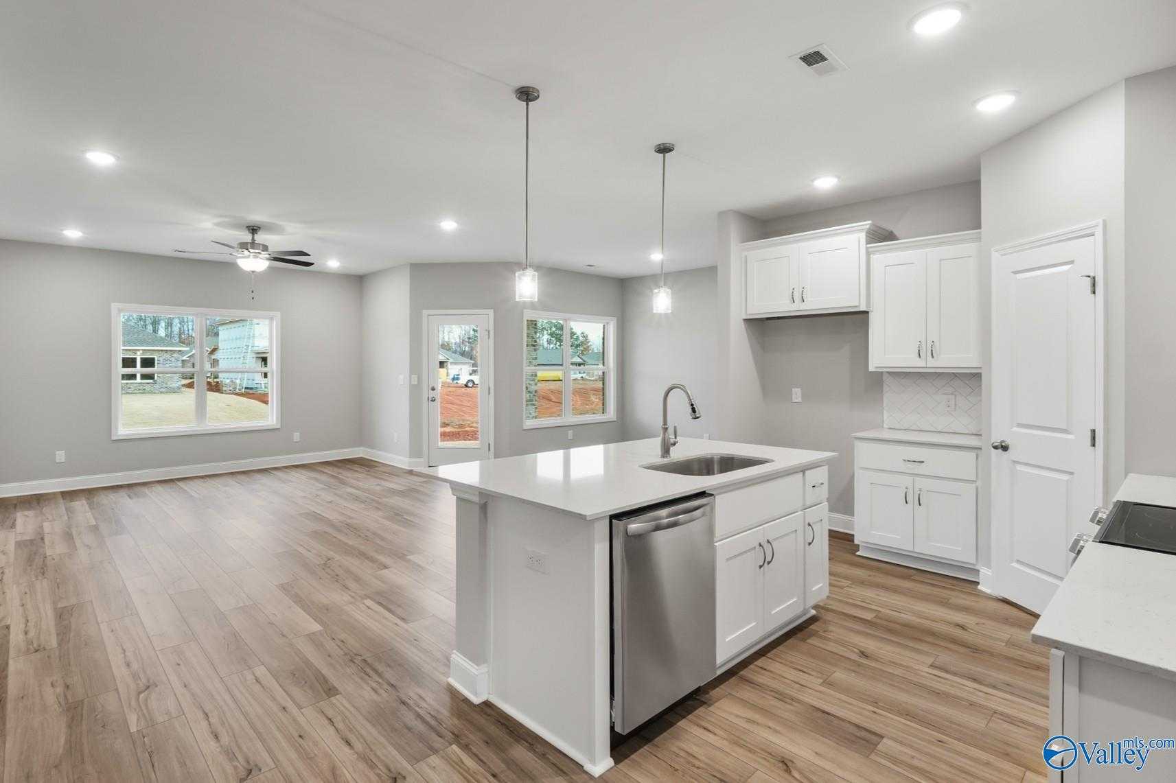 Modern open-concept kitchen with white cabinets, stainless island sink, and hardwood floors in The Daphne D home, Athens AL