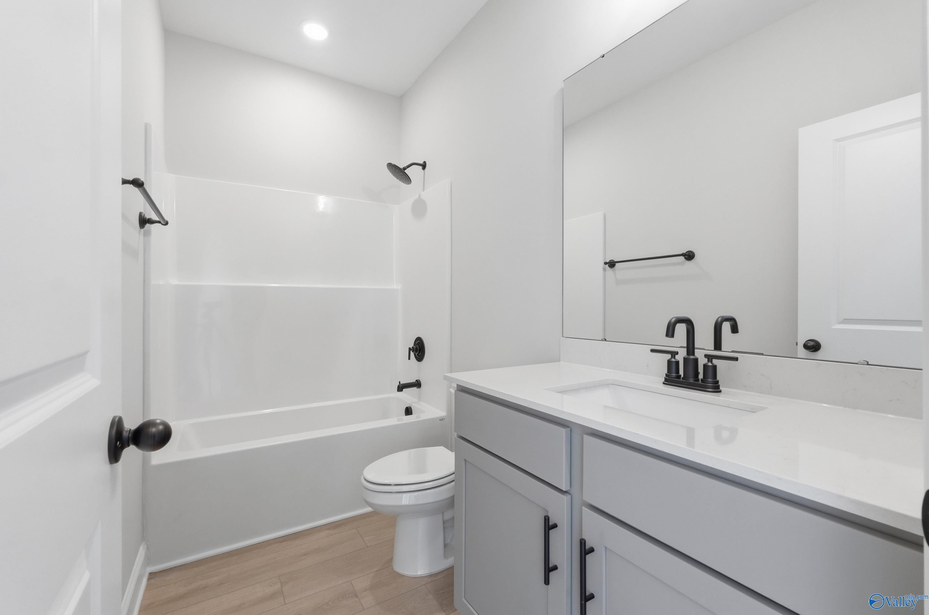 Modern guest bathroom with white tub shower, gray vanity, large mirror in Davidson Homes The Franklin C, New Market, Alabama