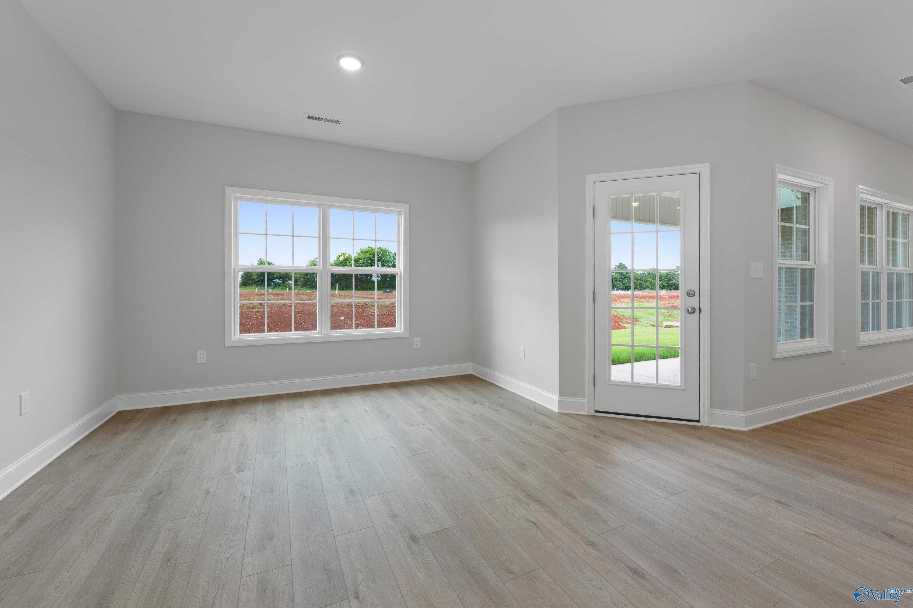 Bright family room with hardwood floors, large windows, and glass door to green backyard in Davidson Homes The Rockford B, Toney, AL