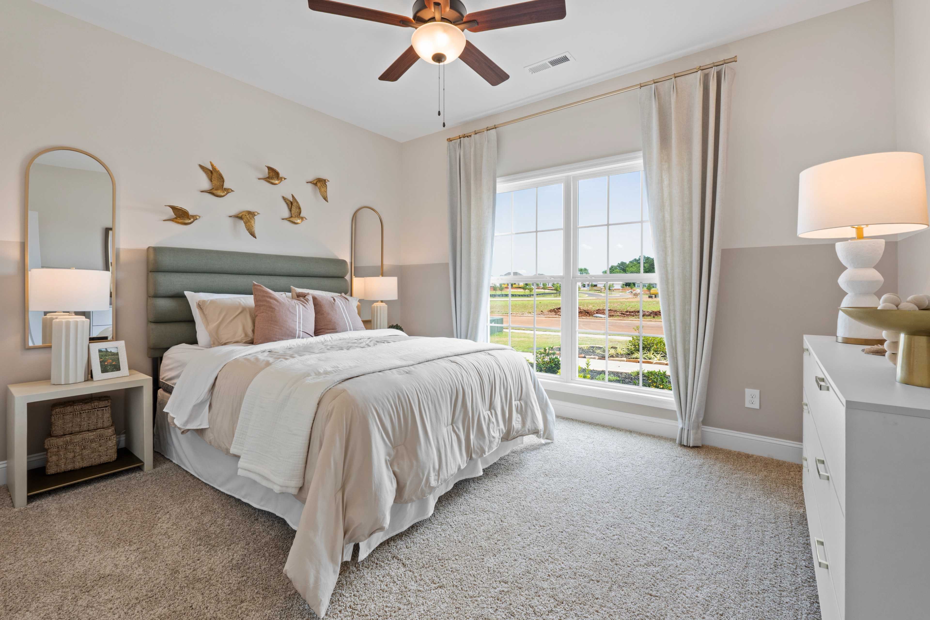 Serene master bedroom in The Daphne with teal upholstered headboard, pink pillows, ceiling fan, and large window view