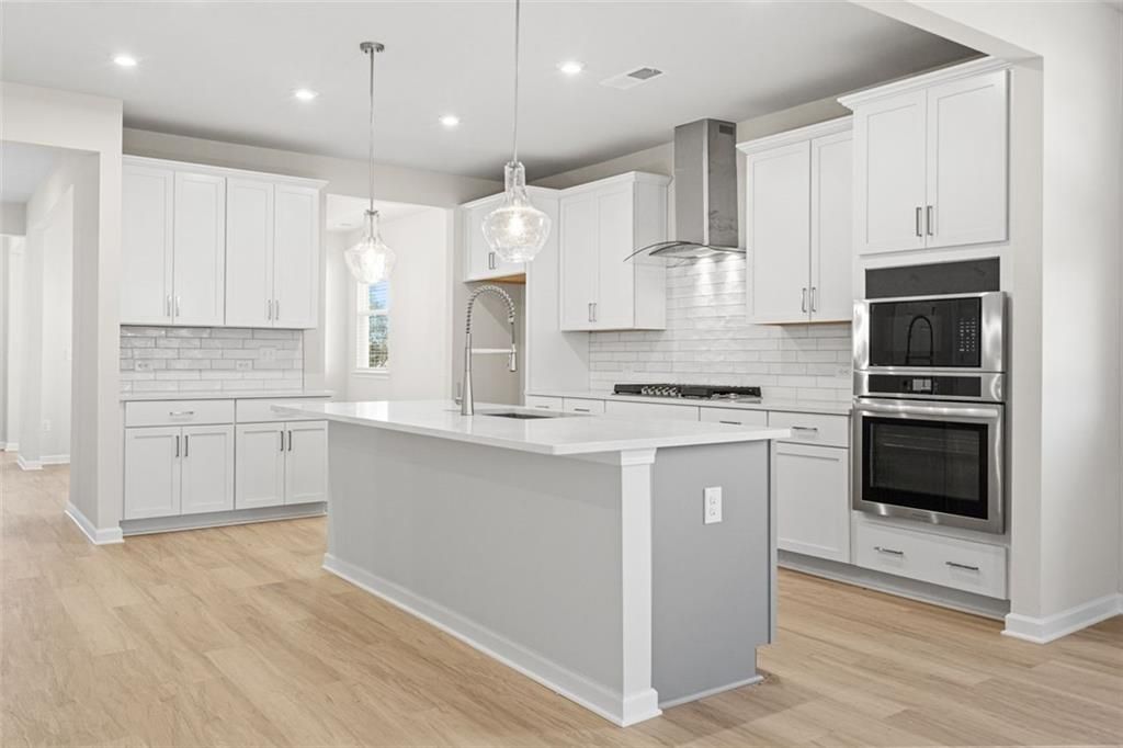 Modern kitchen with white cabinets, gray island, subway tile backsplash, and stainless appliances in The Glenwood C at Wehunt Meadows, Hoschton