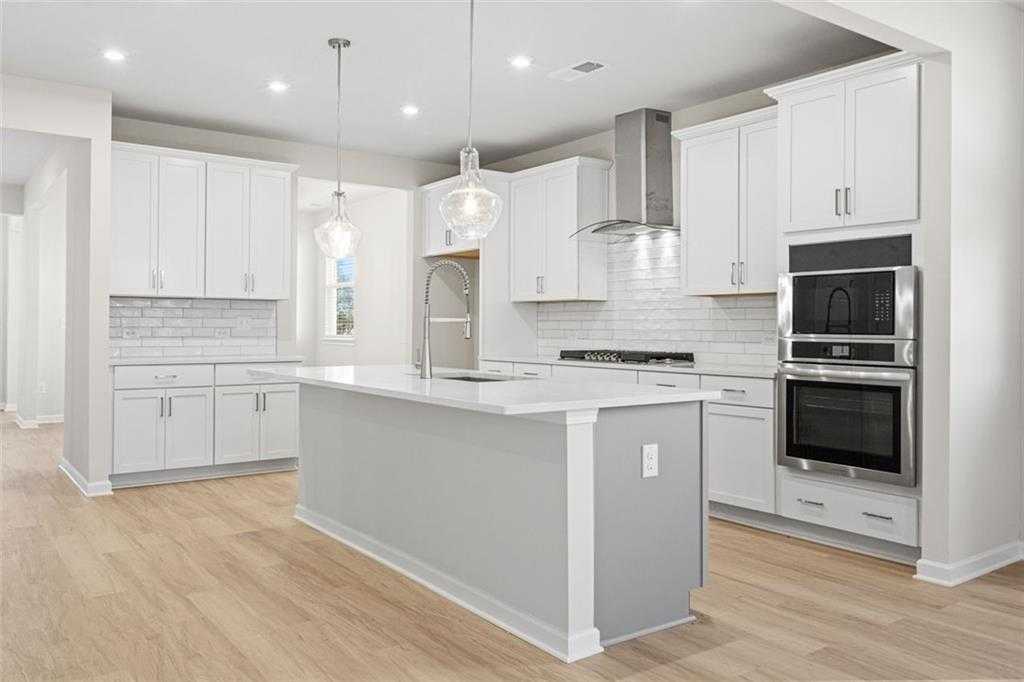 Modern kitchen with white cabinets, gray island, subway tile backsplash, and stainless appliances in The Glenwood C at Wehunt Meadows, Hoschton