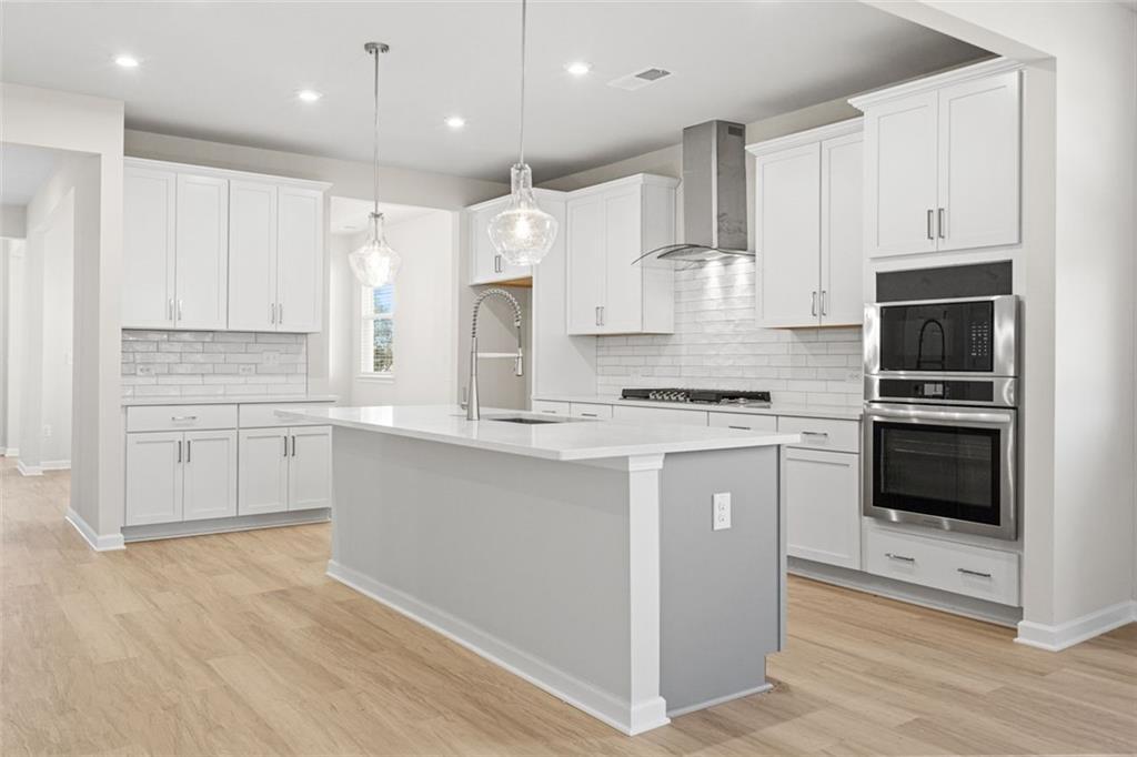 Modern kitchen with white cabinets, gray island, subway tile backsplash, and stainless appliances in The Glenwood C at Wehunt Meadows, Hoschton
