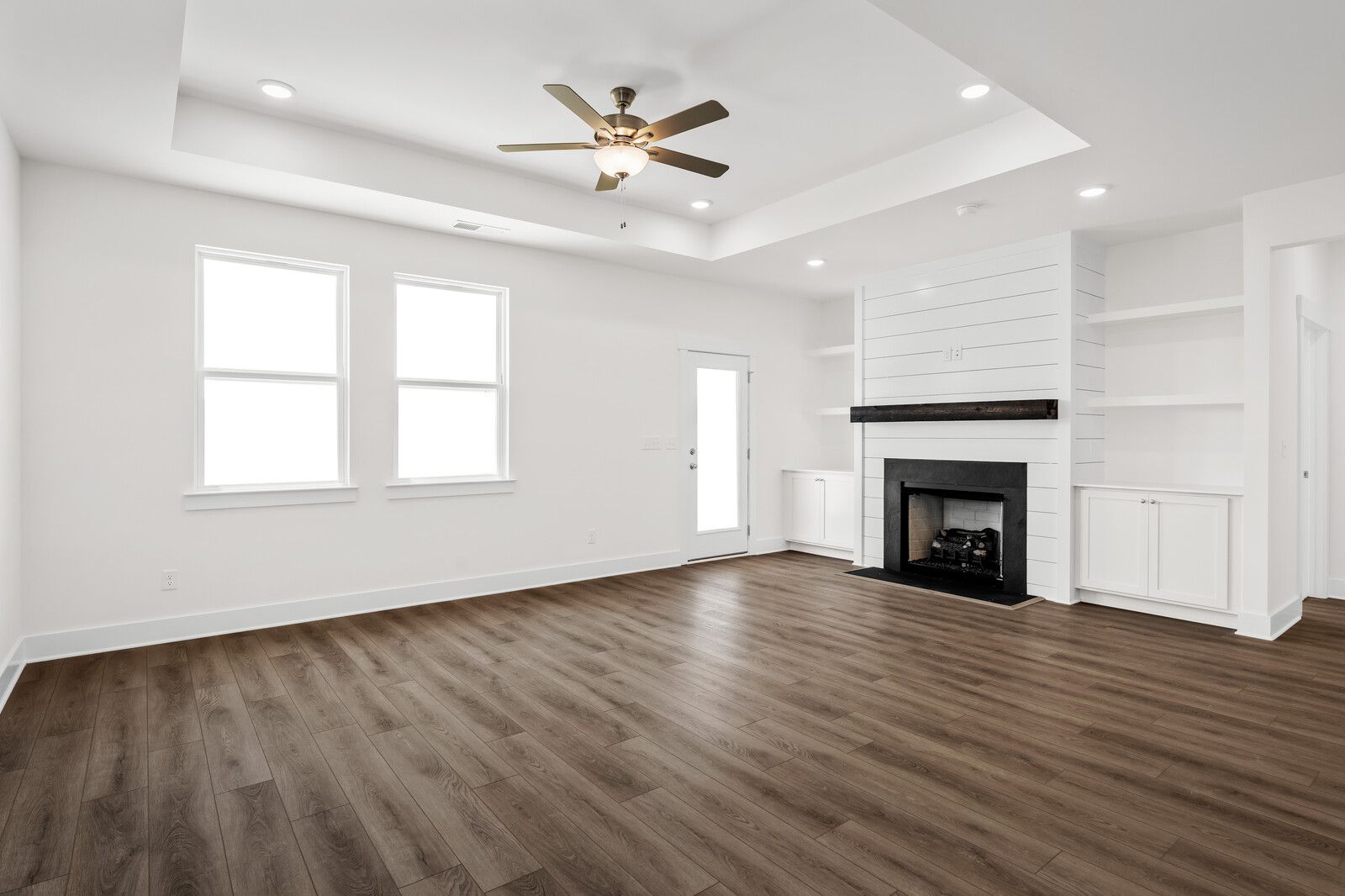 Bright, open-concept living room in The Cottonwood floor plan featuring a shiplap fireplace, tray ceiling, and wood floors.