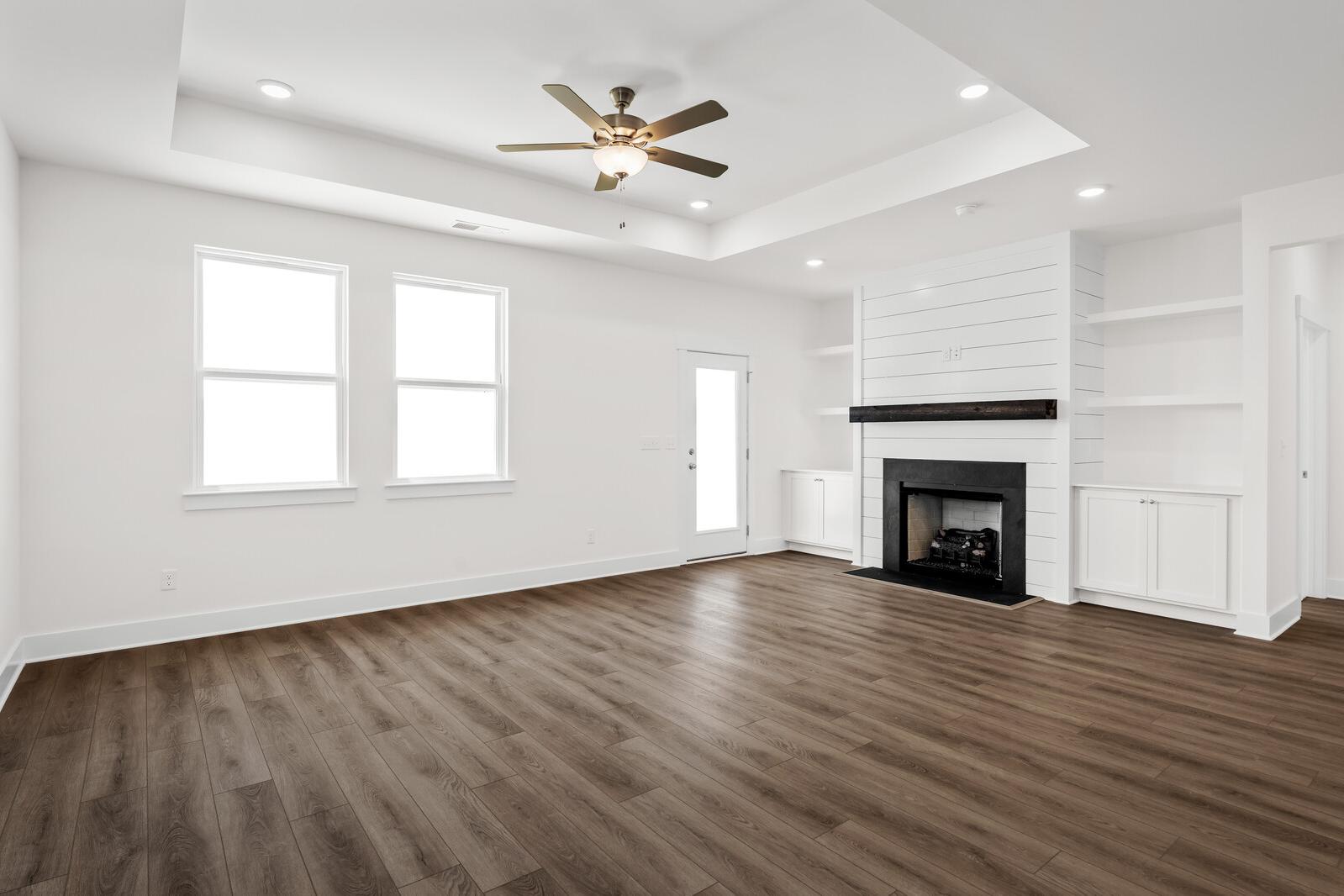 Bright, open-concept living room in The Cottonwood floor plan featuring a shiplap fireplace, tray ceiling, and wood floors.