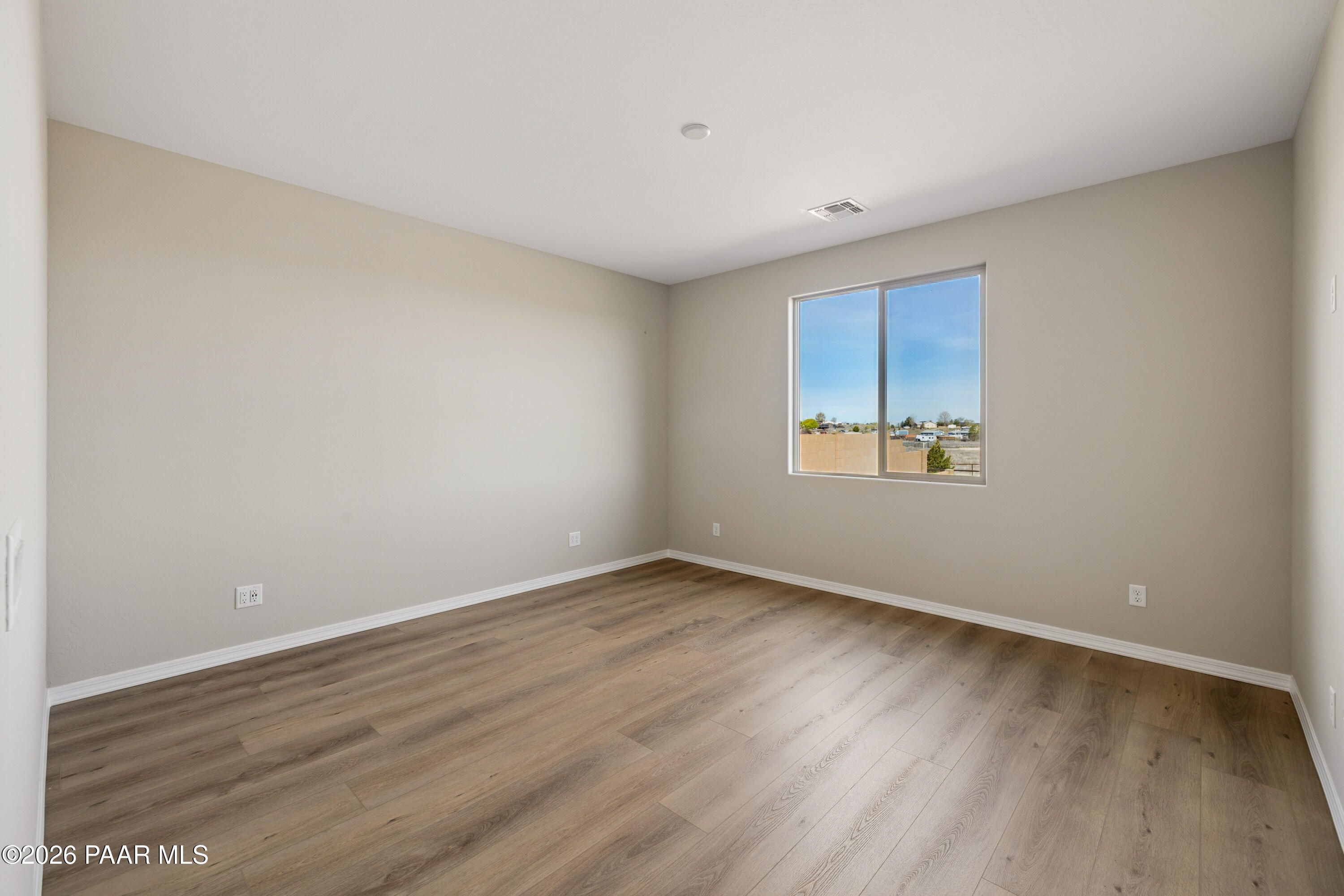 Bright empty bedroom with beige walls, light wood floors, and large window overlooking Arizona desert in Davidson Homes The Harmony A, Prescott Valley