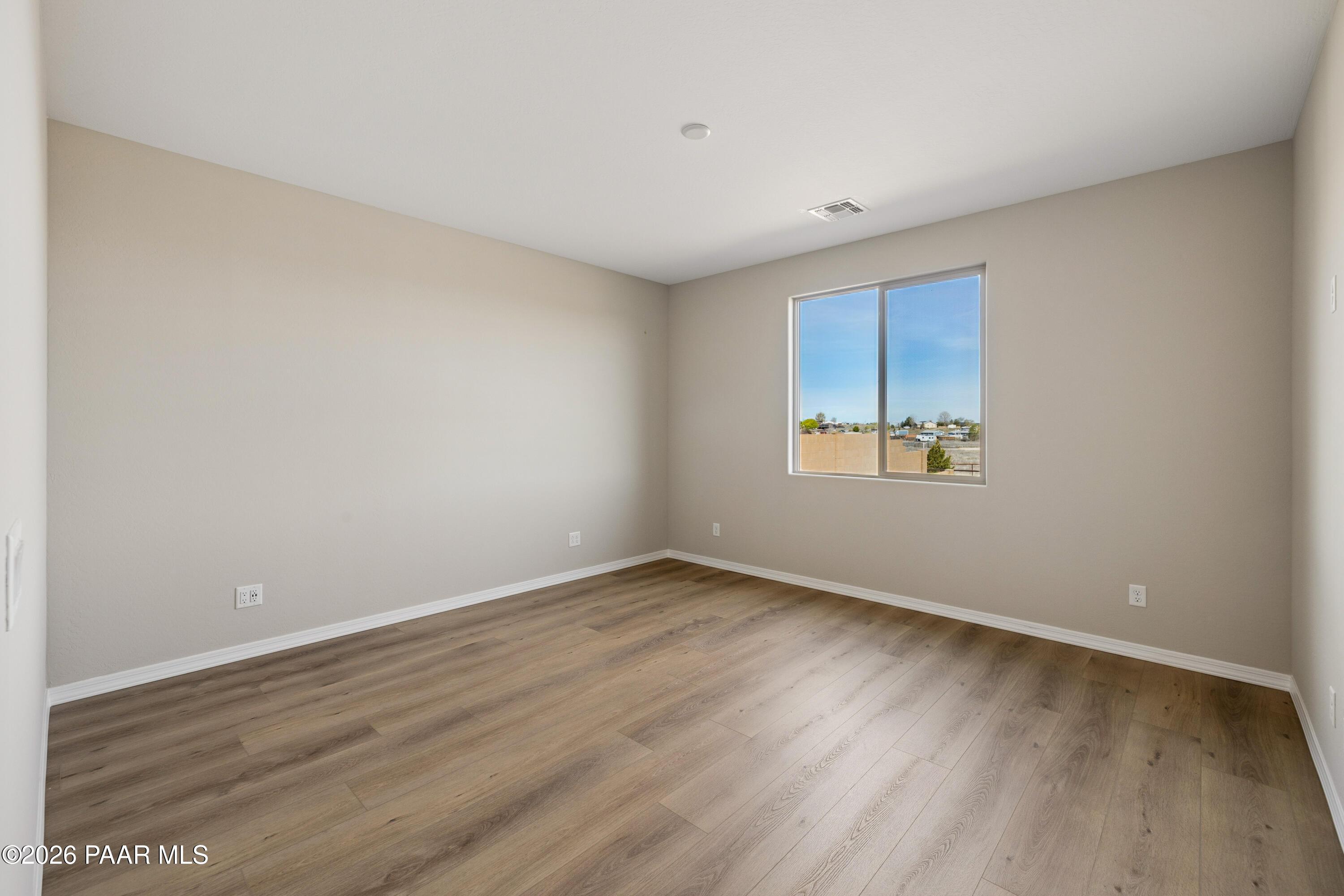 Bright empty bedroom with beige walls, light wood floors, and large window overlooking Arizona desert in Davidson Homes The Harmony A, Prescott Valley
