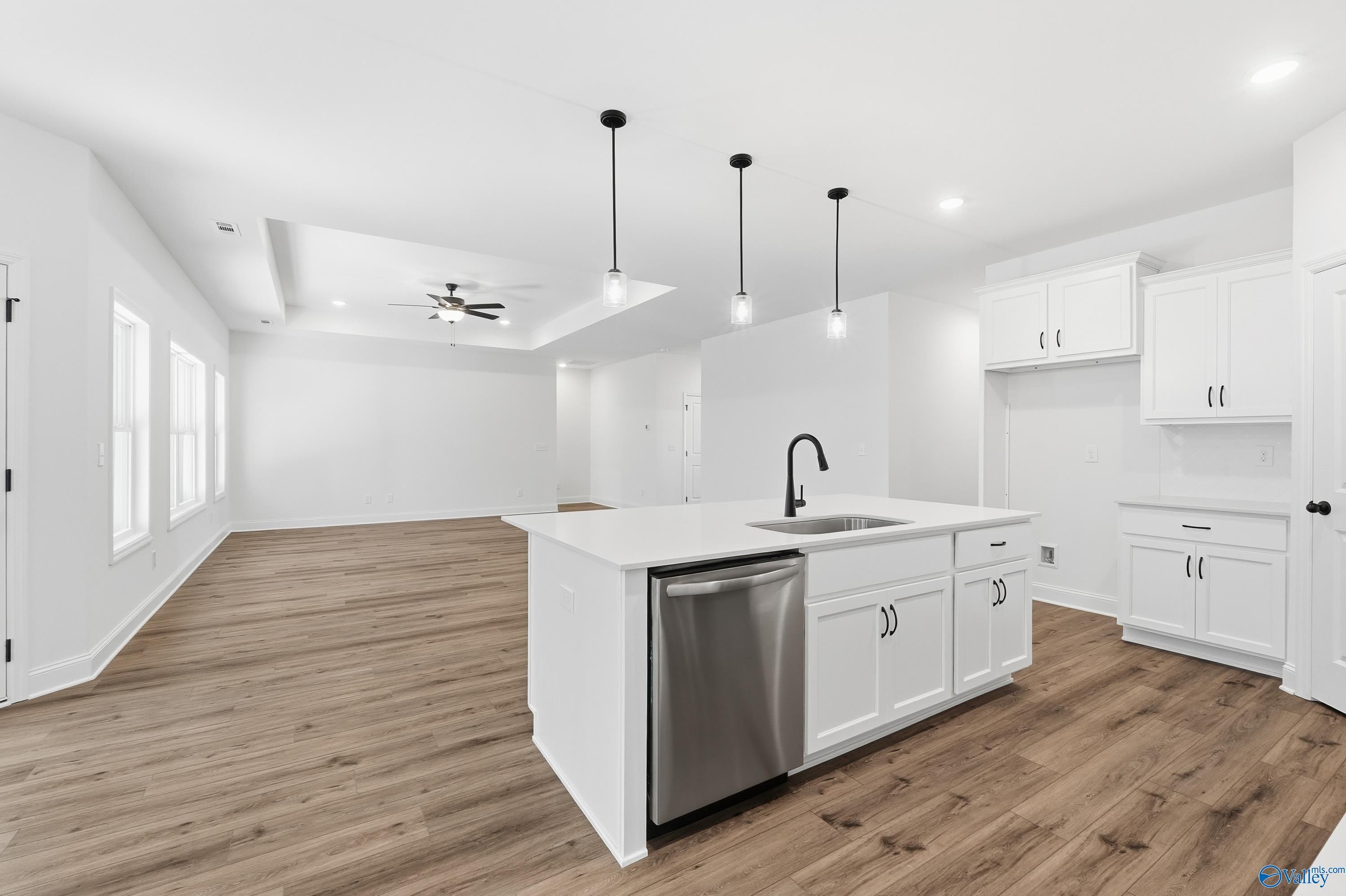 Modern open-concept kitchen with white island sink, stainless dishwasher, pendant lights, and hardwood floors in The Rockford D, Hazel Green, AL