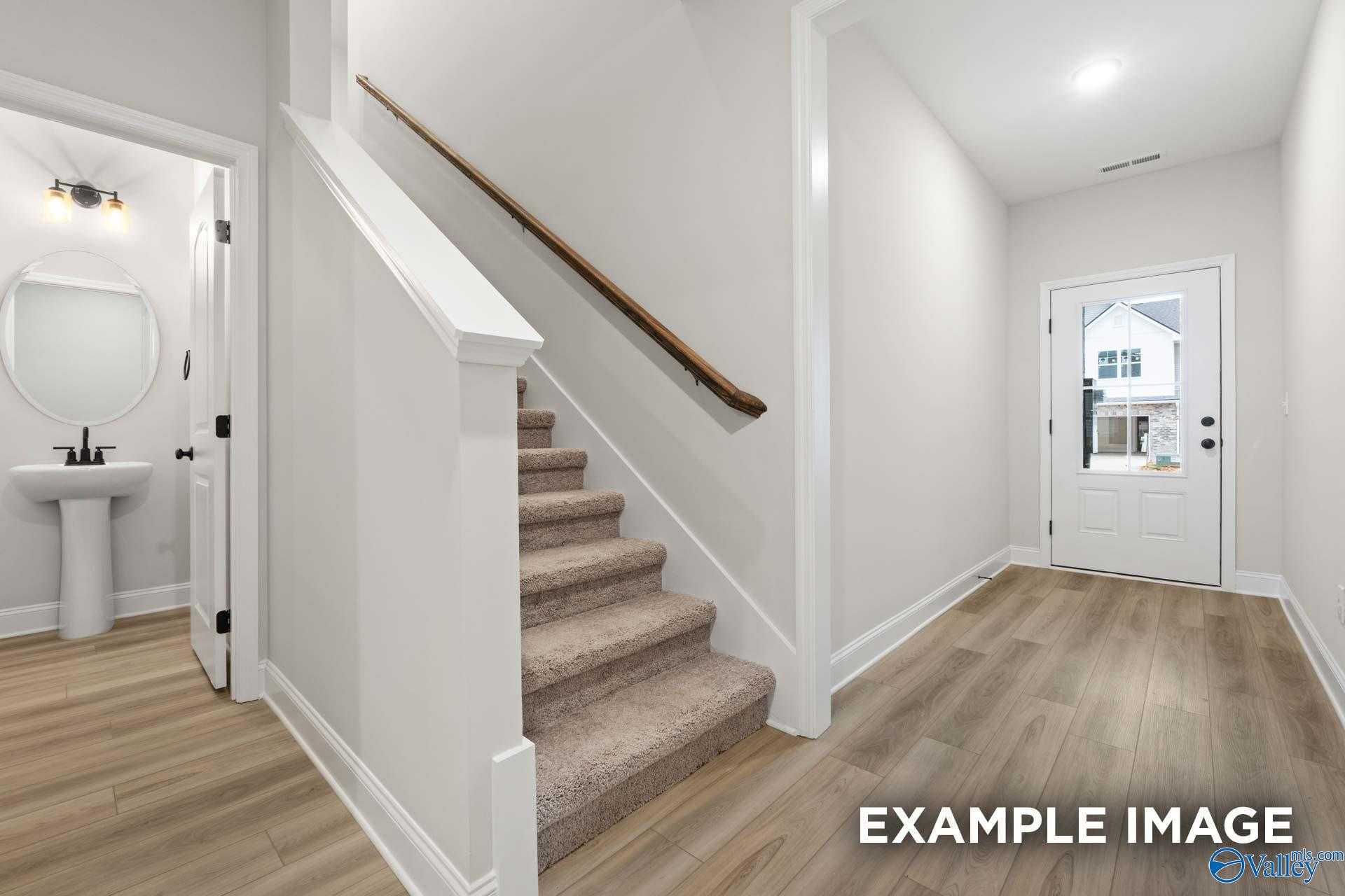 Bright entry foyer with carpeted staircase, powder room, and glass back door in Davidson Homes The Camden D, Huntsville, Alabama