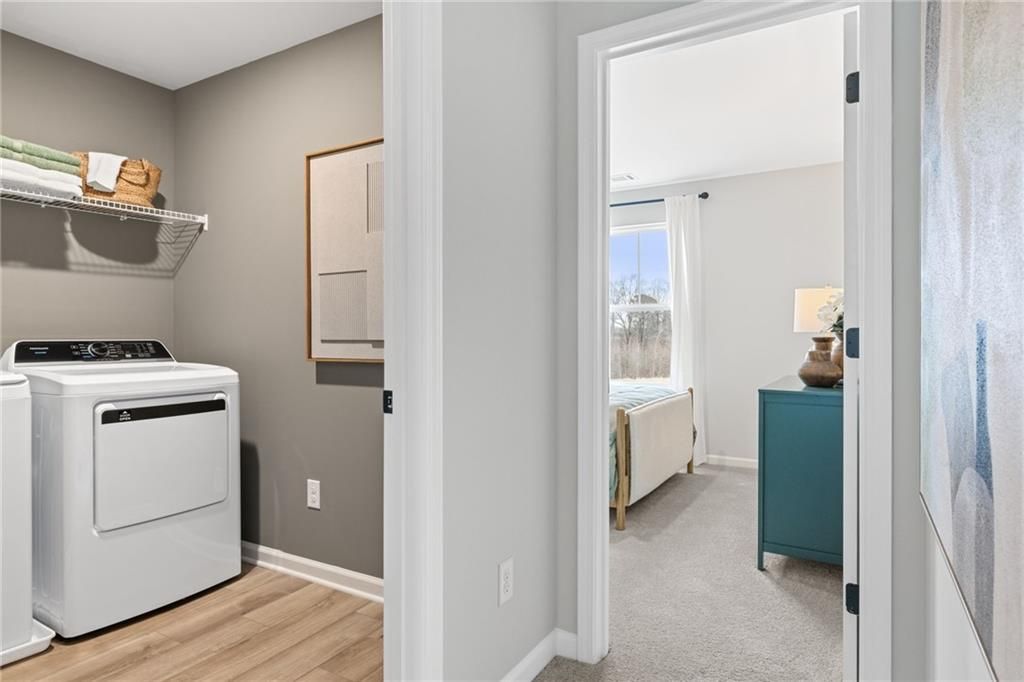 Laundry room with white washer and dryer adjacent to a carpeted bedroom in The Rabun B floor plan, The Bluffs, Canton, GA.