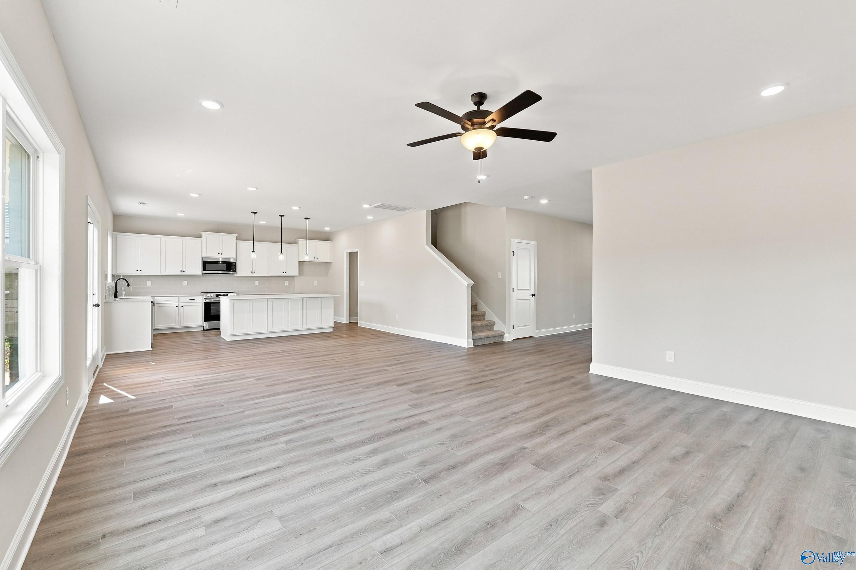 Open-concept living area with luxury vinyl plank flooring, white kitchen, and ceiling fan in Davidson Homes Chelsea B, New Market, AL