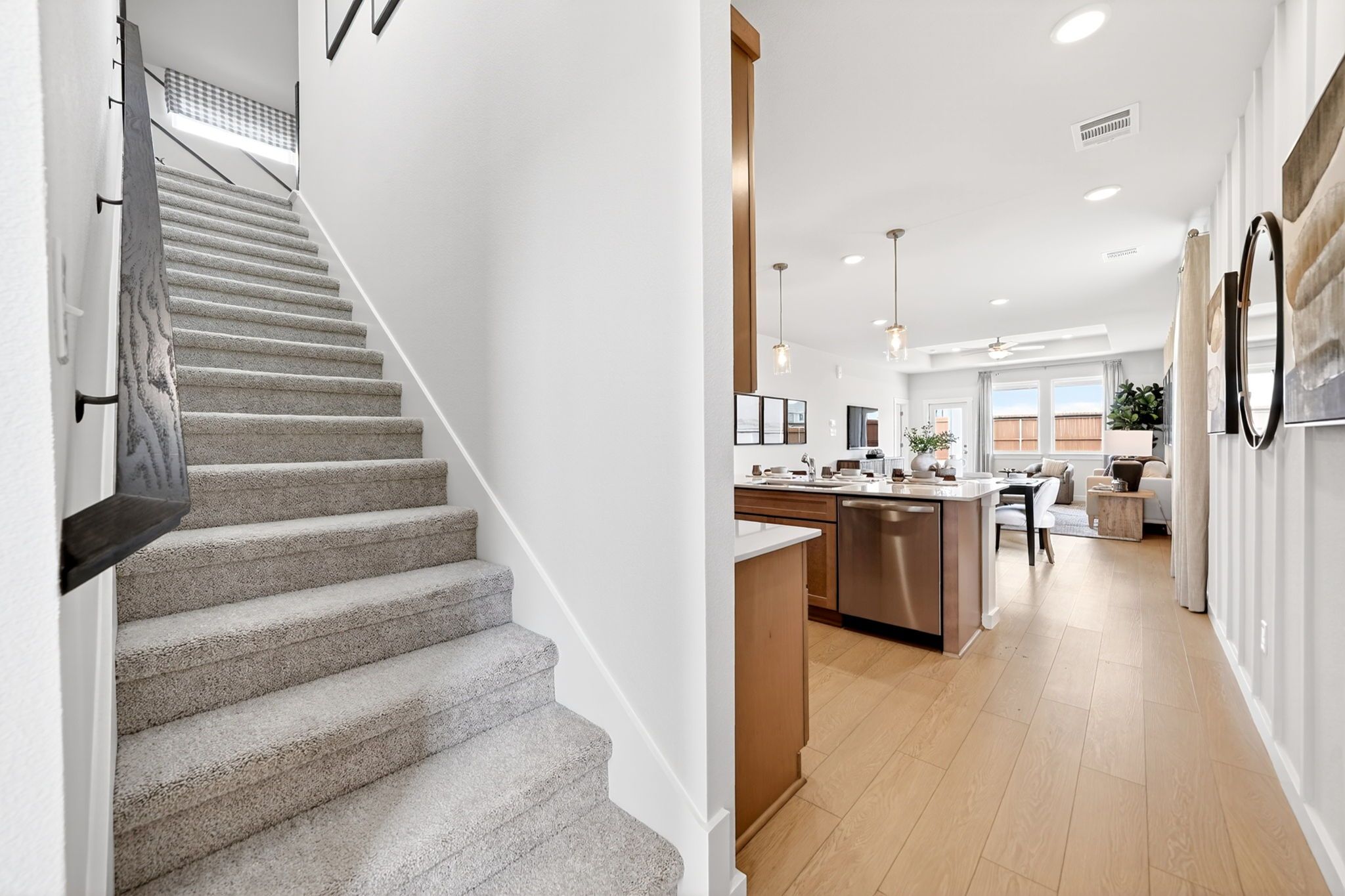 Open-concept kitchen and living area with carpeted staircase in Heartland Texas Davidson Homes featuring wood floors, island, and large windows