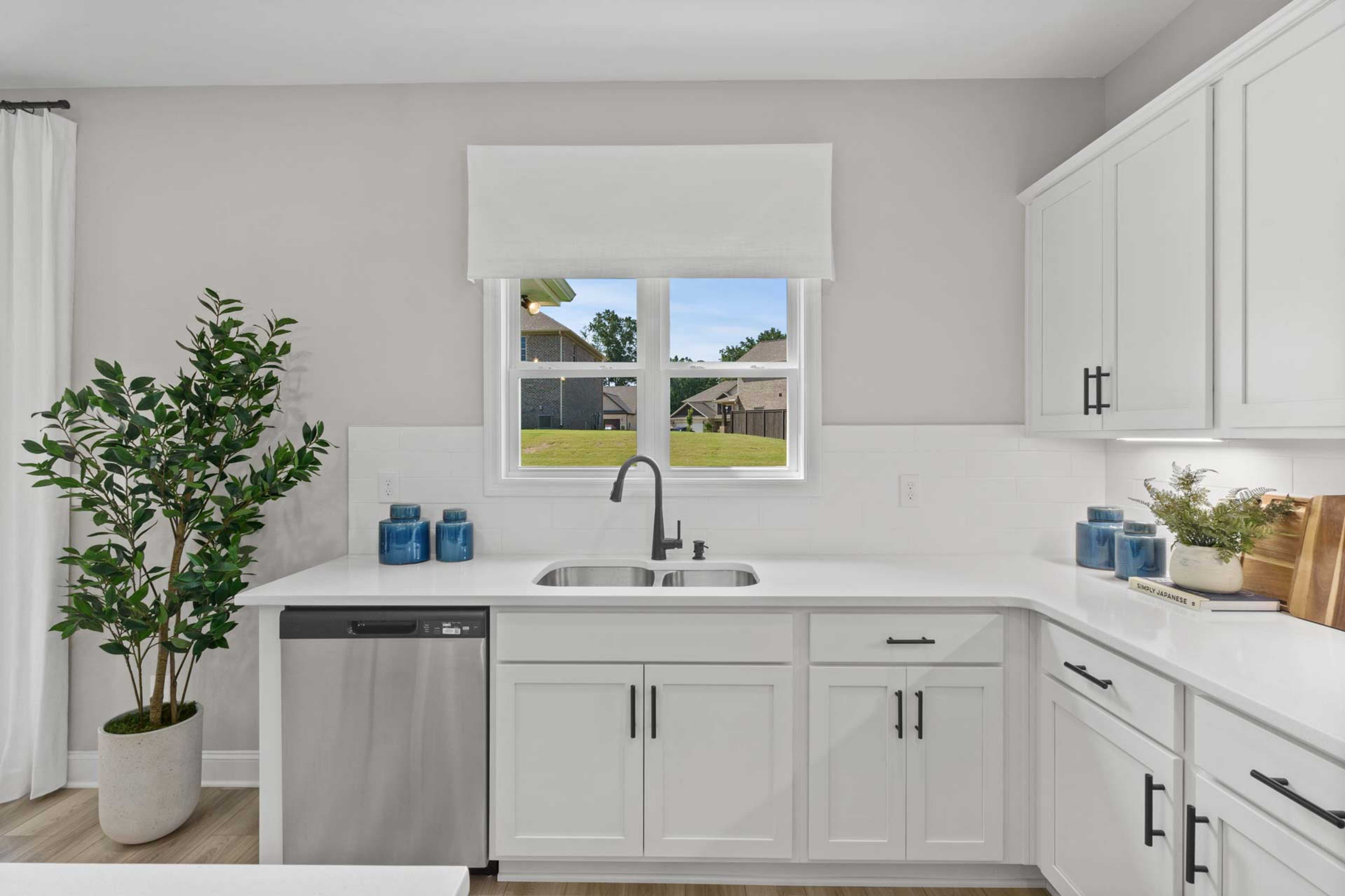 Spacious white kitchen at Creek Grove in New Market Alabama with shaker cabinets, quartz counters, stainless sink and backyard view